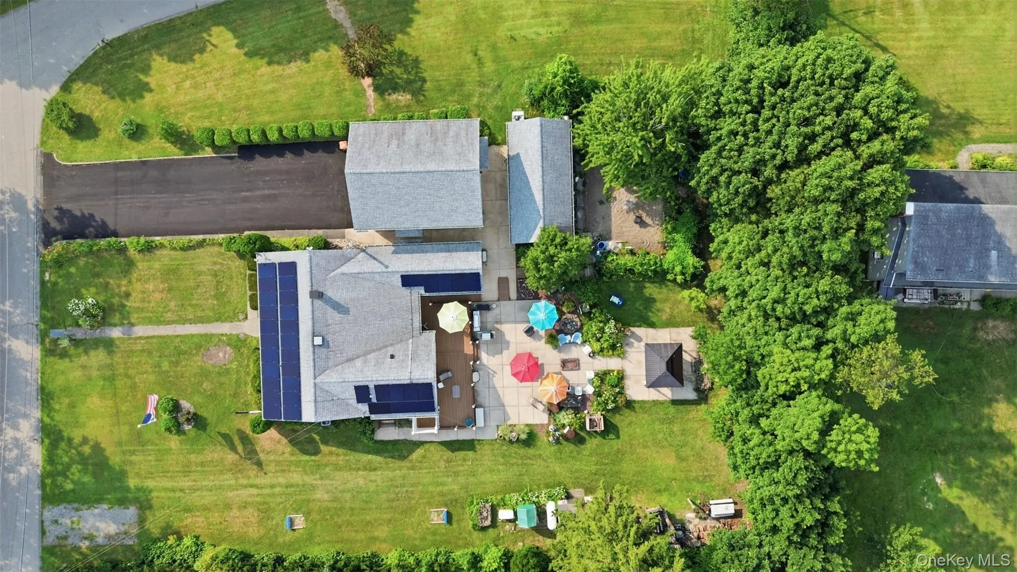Expansive property featuring a main residence with solar panels, a detached garage, and a large paved driveway Expansive property featuring a main residence with solar panels, a detached garage, and a large paved driveway