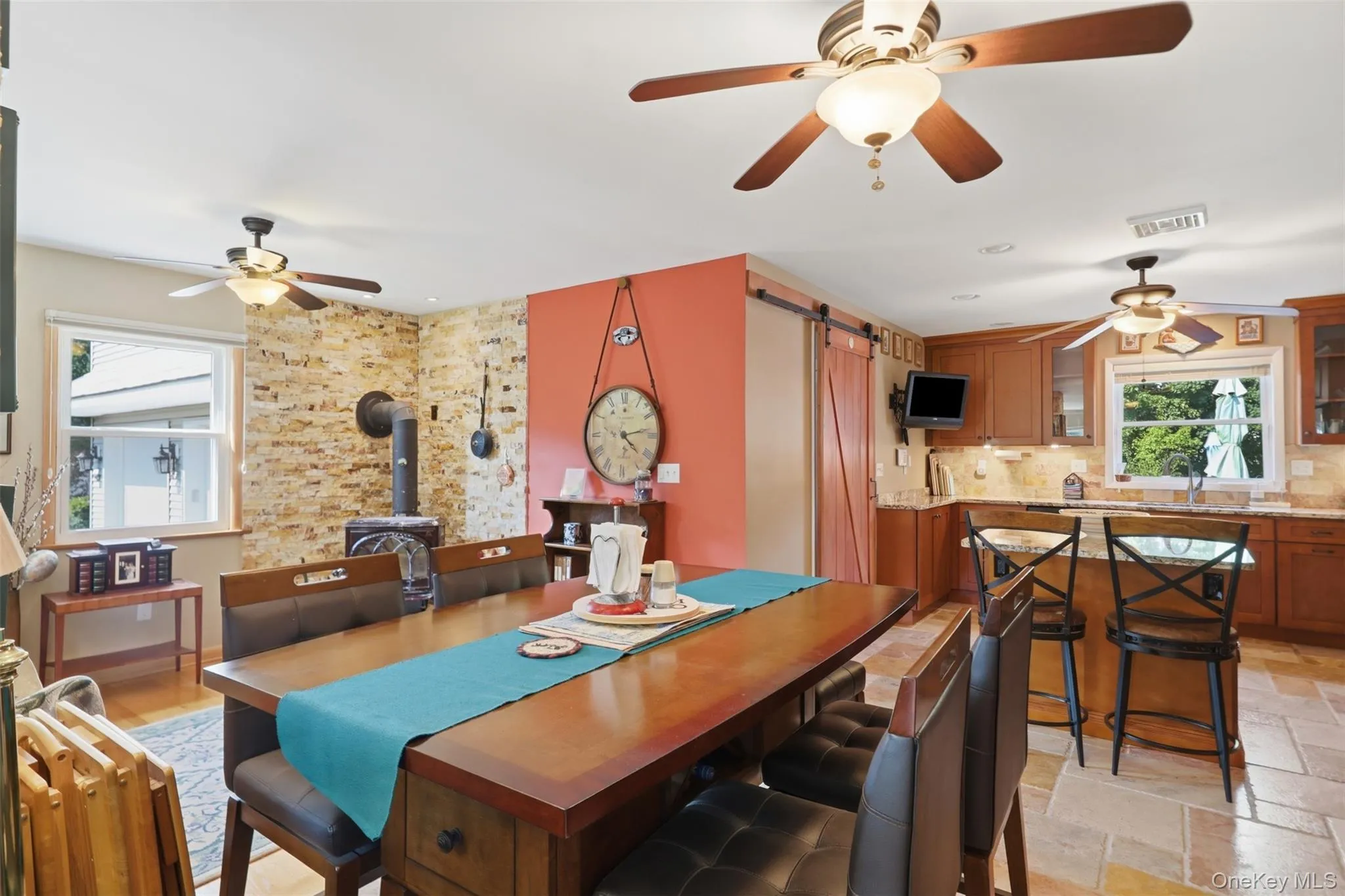 Open-concept room featuring a wood-burning stove, exposed brick accent wall, and wood-finish flooring Open-concept room featuring a wood-burning stove, exposed brick accent wall, and wood-finish flooring