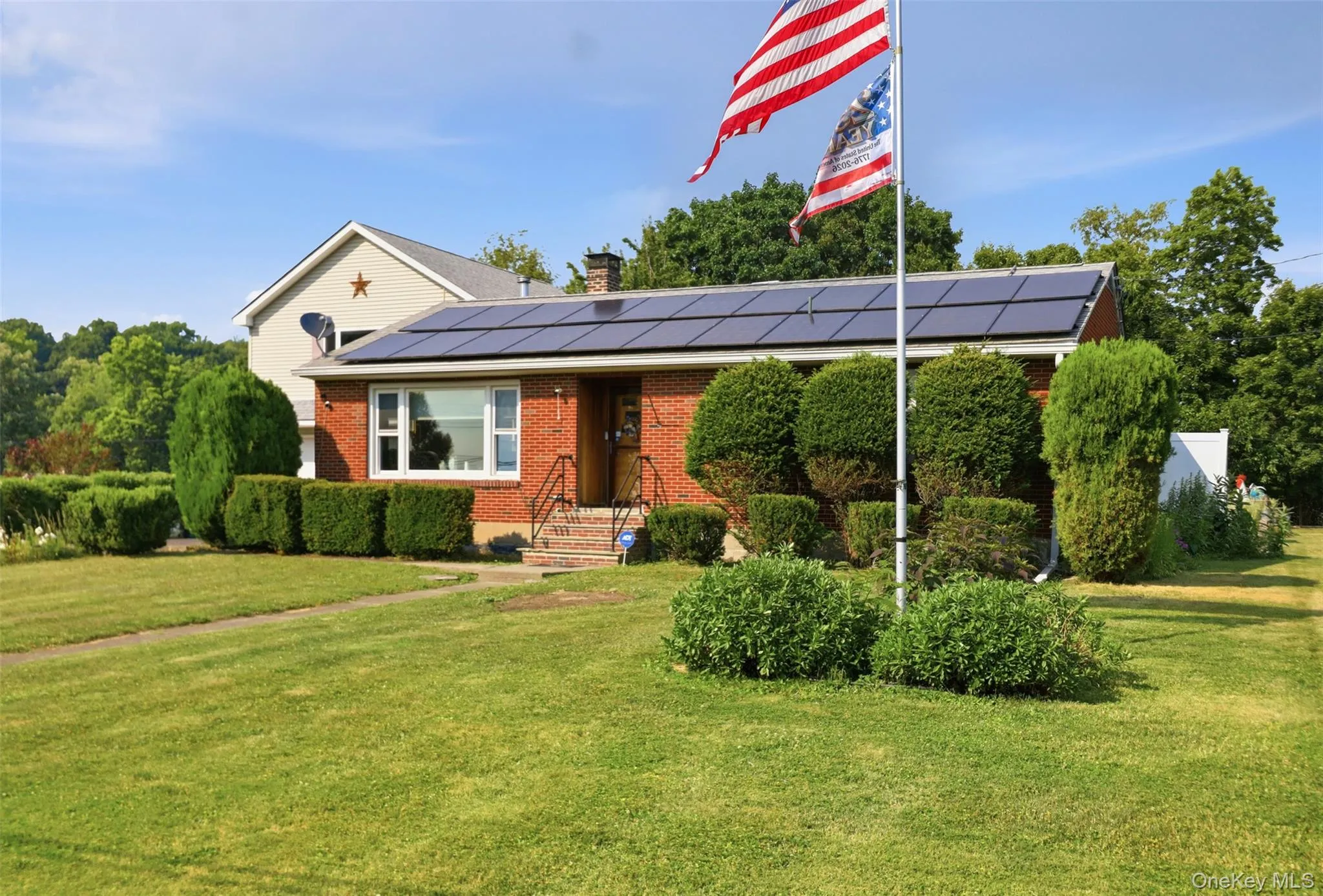 Brick facade residence featuring solar panels, a gabled roofline, and mature landscaping Brick facade residence featuring solar panels, a gabled roofline, and mature landscaping