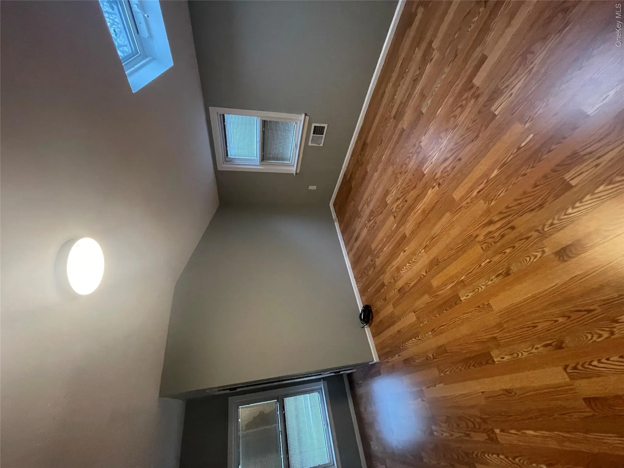 Empty room with baseboards, vaulted ceiling with skylight, visible vents, and wood finished floors Empty room with baseboards, vaulted ceiling with skylight, visible vents, and wood finished floors