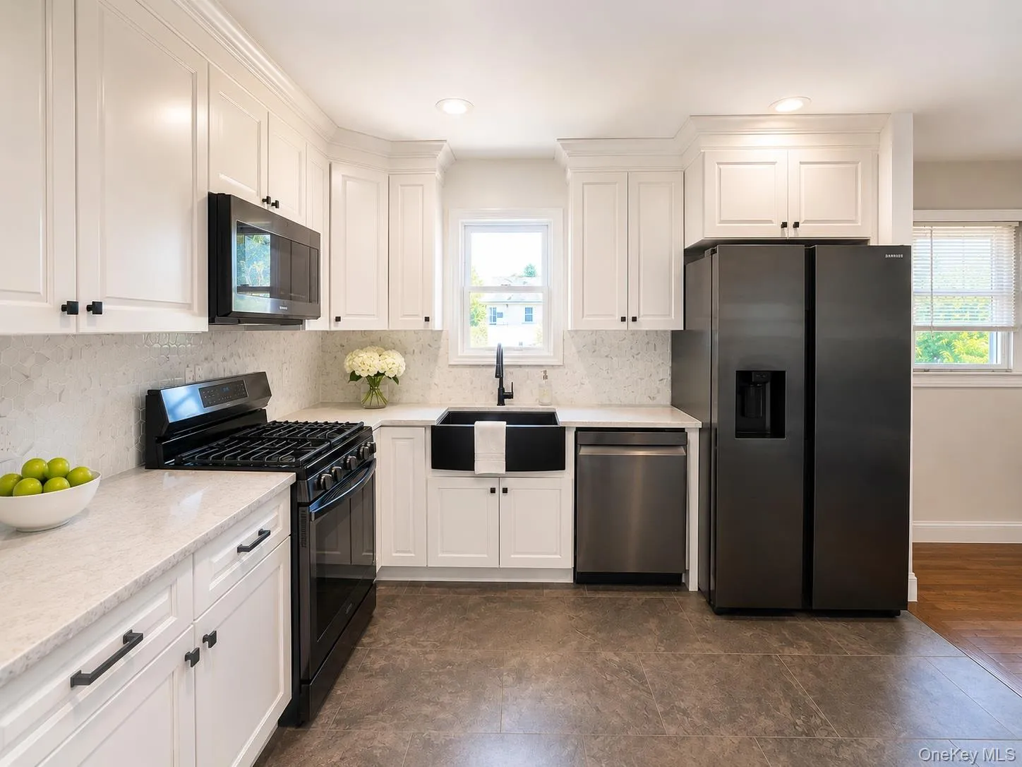 Kitchen featuring white cabinetry with dark hardware, a white tile backsplash, and light-toned countertops Kitchen featuring white cabinetry with dark hardware, a white tile backsplash, and light-toned countertops