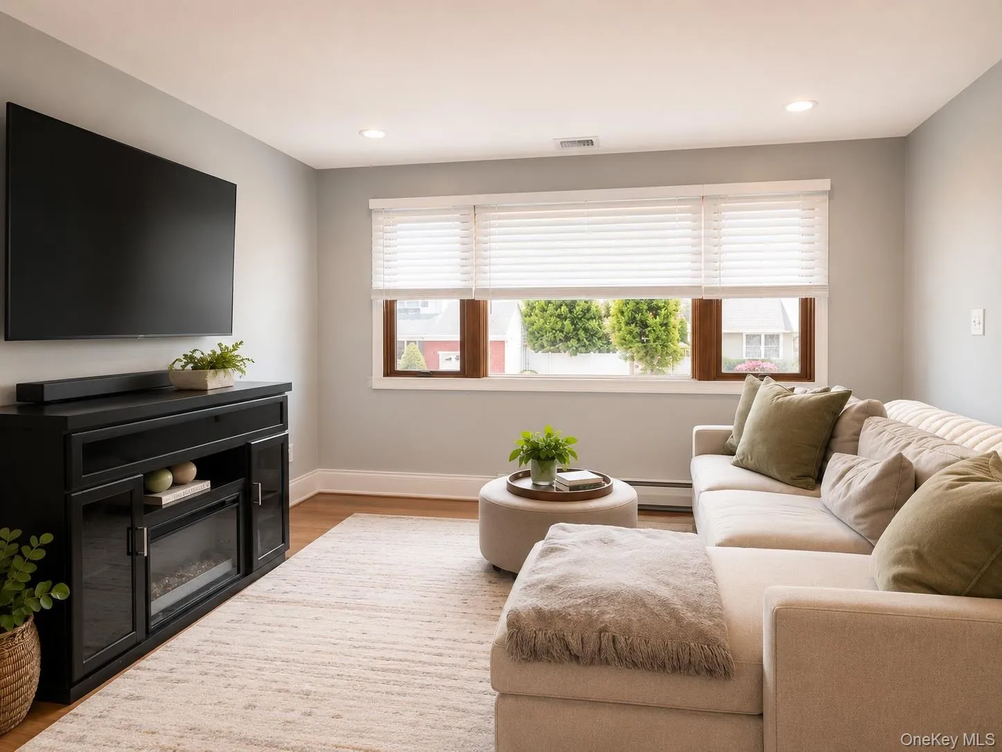 Living room featuring wood-finish flooring, recessed lighting, and a wall-mounted media console with an integrated electric fireplace Living room featuring wood-finish flooring, recessed lighting, and a wall-mounted media console with an integrated electric fireplace
