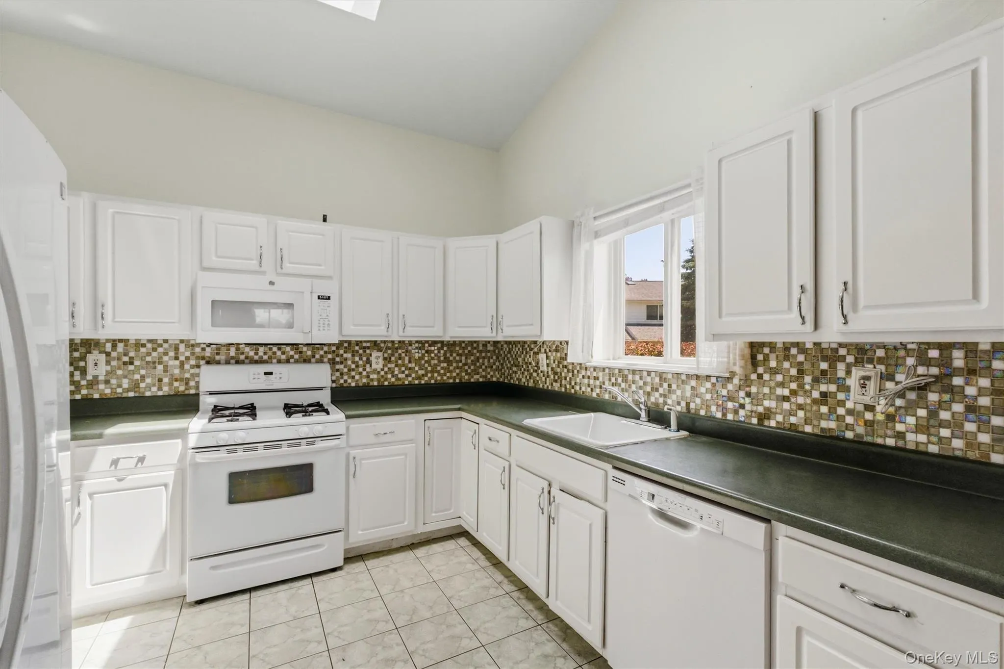 Kitchen featuring white cabinetry, a mosaic tile backsplash, dark countertops, and tile flooring Kitchen featuring white cabinetry, a mosaic tile backsplash, dark countertops, and tile flooring