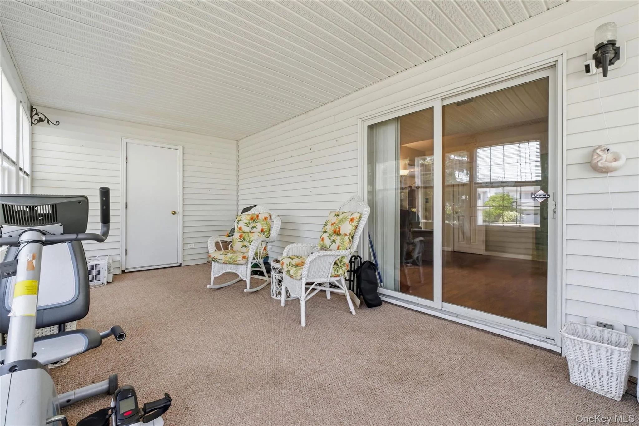 Enclosed porch featuring multiple windows, white vinyl siding, textured carpet, and a sliding glass door Enclosed porch featuring multiple windows, white vinyl siding, textured carpet, and a sliding glass door