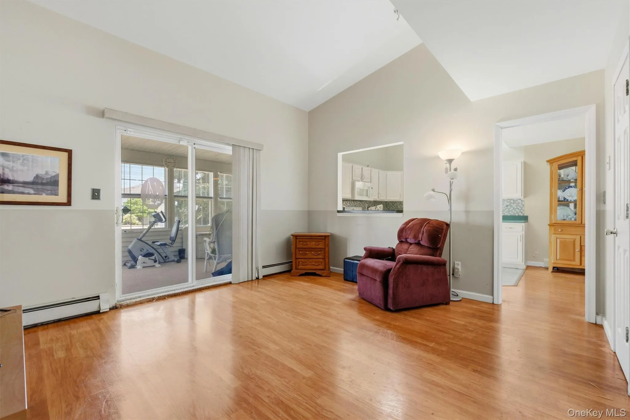 Spacious living area featuring wood-finish flooring, vaulted ceilings, and sliding glass doors opening to a sunroom Spacious living area featuring wood-finish flooring, vaulted ceilings, and sliding glass doors opening to a sunroom