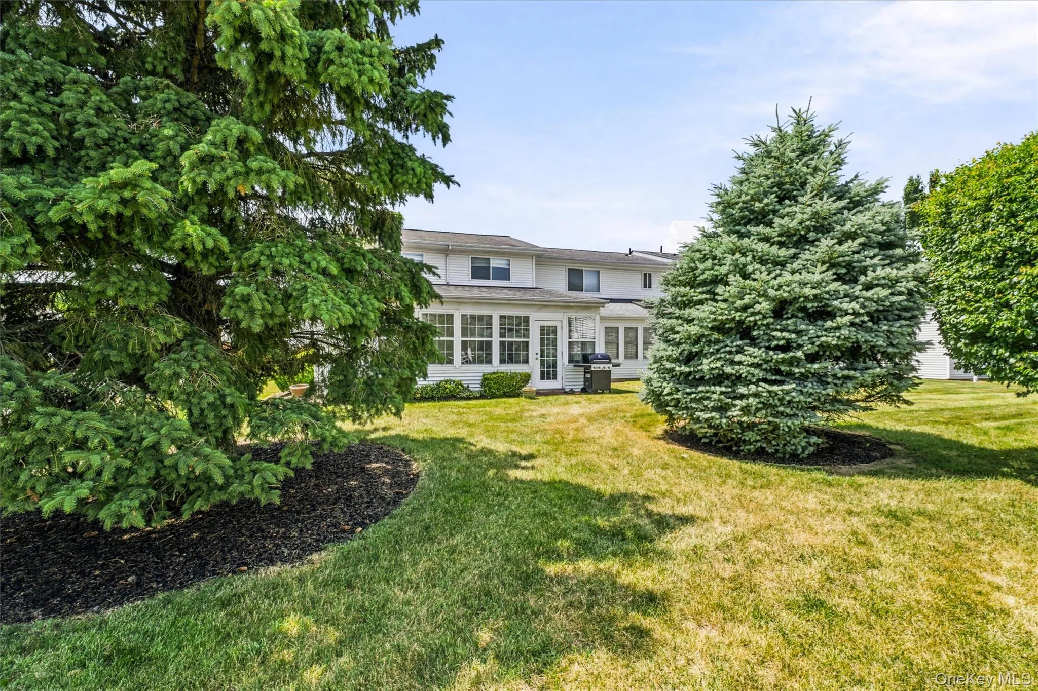 Rear exterior featuring a spacious shared green space, mature landscaping, and a screened-in porch for outdoor enjoyment Rear exterior featuring a spacious shared green space, mature landscaping, and a screened-in porch for outdoor enjoyment