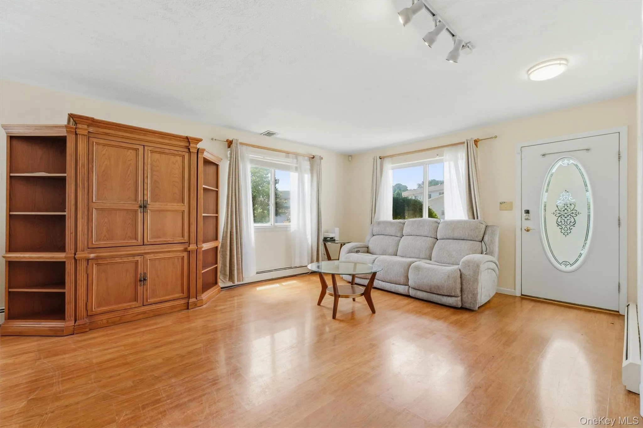 Bright and spacious living room featuring hardwood floors, abundant natural light, and large windows. The open layout offers plenty of space for seating and includes a front entry with an adjacent dining area Bright and spacious living room featuring hardwood floors, abundant natural light, and large windows. The open layout offers plenty of space for seating and includes a front entry with an adjacent dining area