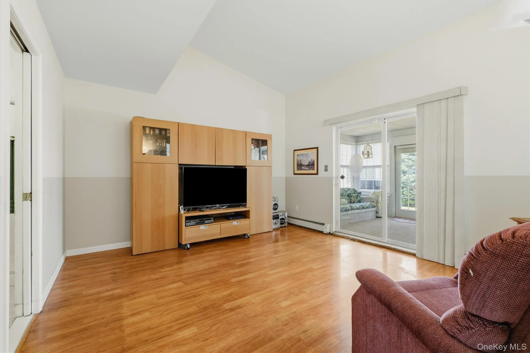Living area featuring wood-finish flooring, a vaulted ceiling, and sliding glass doors to an enclosed porch Living area featuring wood-finish flooring, a vaulted ceiling, and sliding glass doors to an enclosed porch