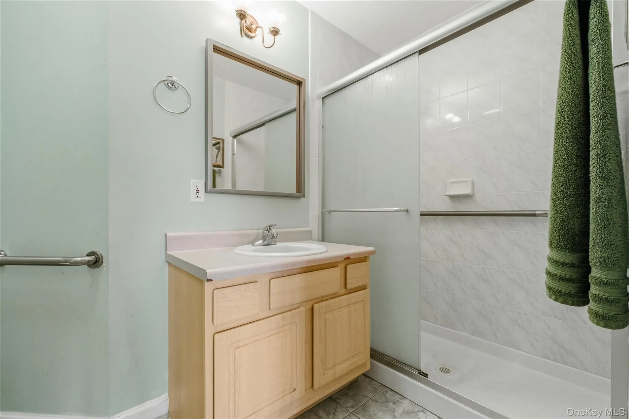 Bathroom featuring a single vanity with light-colored cabinetry, a rectangular mirror, a shower with sliding glass doors, and tiled walls in the shower enclosure Bathroom featuring a single vanity with light-colored cabinetry, a rectangular mirror, a shower with sliding glass doors, and tiled walls in the shower enclosure
