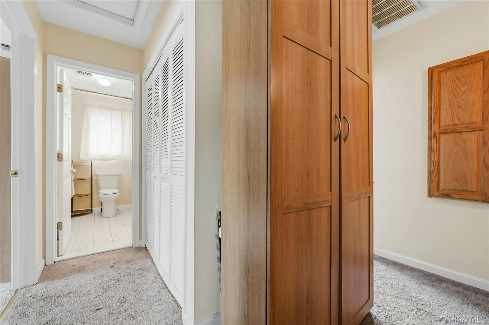 Hallway featuring a built-in wood-finish wardrobe, a louvered bi-fold door, and carpet flooring Hallway featuring a built-in wood-finish wardrobe, a louvered bi-fold door, and carpet flooring