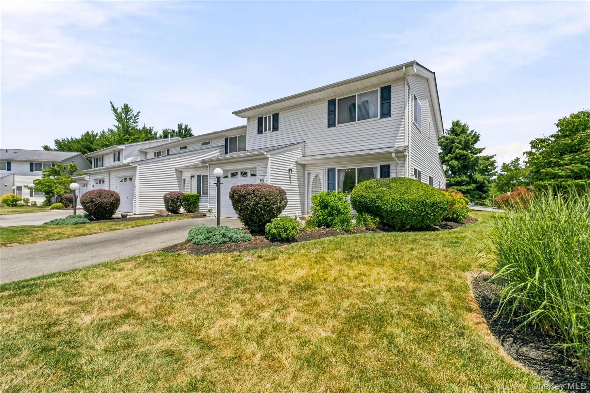 White-sided townhome featuring a private garage, established landscaping, and a paved driveway White-sided townhome featuring a private garage, established landscaping, and a paved driveway