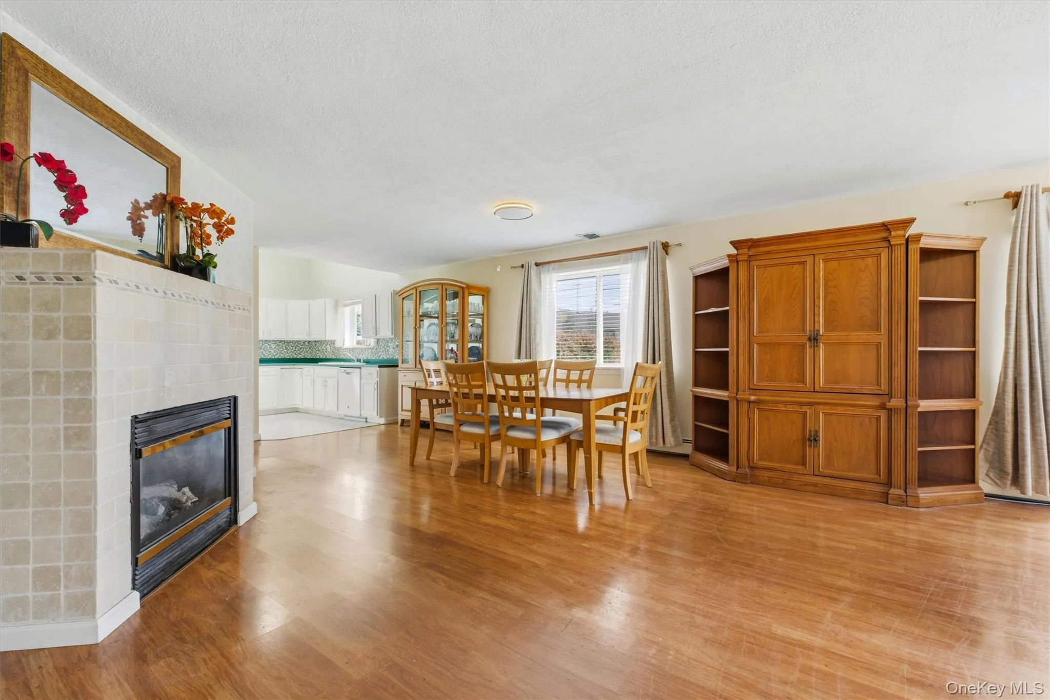 Open-concept living area featuring wood-finish flooring, a tiled fireplace with mantel, and a window with outdoor scenery Open-concept living area featuring wood-finish flooring, a tiled fireplace with mantel, and a window with outdoor scenery