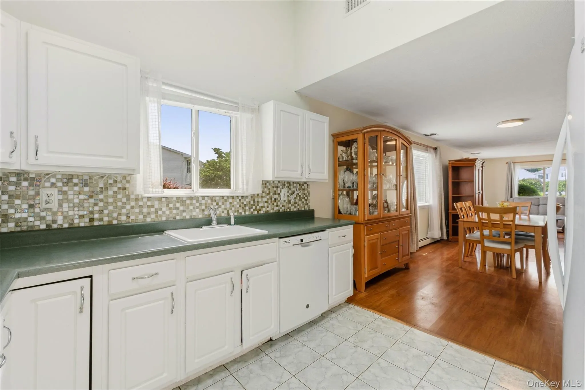 Kitchen featuring white cabinetry, mosaic tile backsplash, solid surface countertops, and a white sink Kitchen featuring white cabinetry, mosaic tile backsplash, solid surface countertops, and a white sink