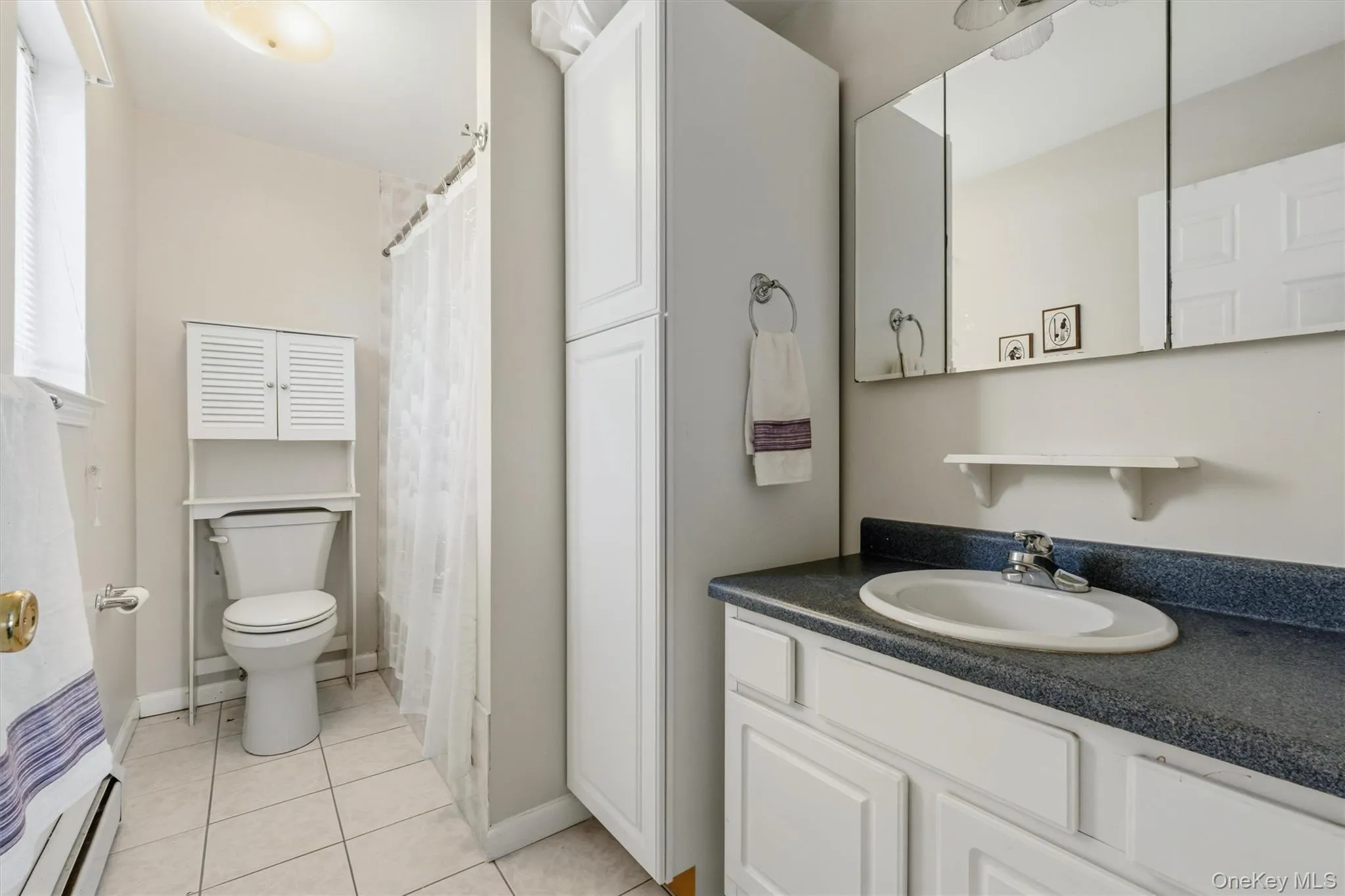 Bathroom vanity with an integrated sink, tri-fold mirrored medicine cabinet, and white paneled cabinetry Bathroom vanity with an integrated sink, tri-fold mirrored medicine cabinet, and white paneled cabinetry