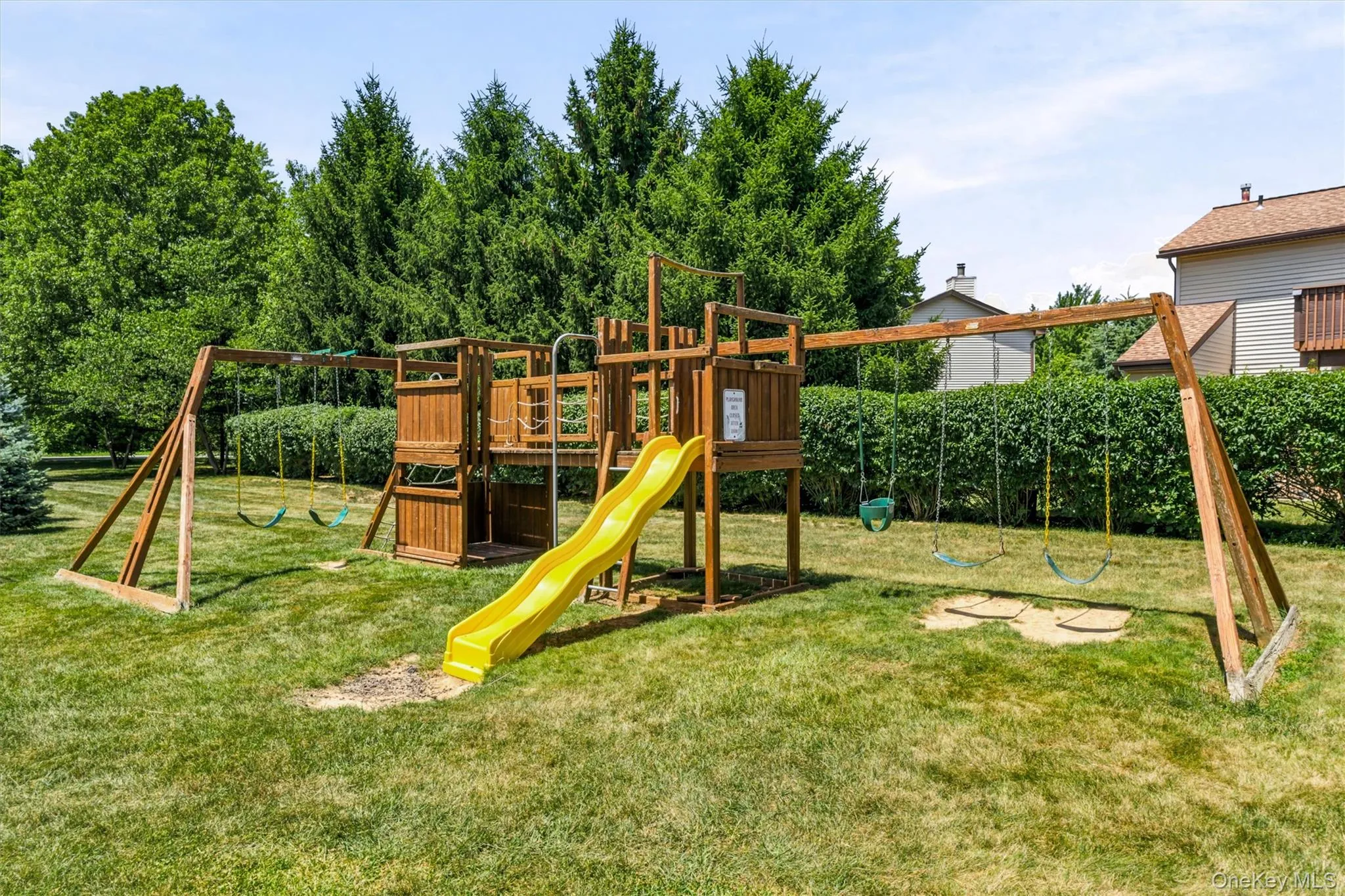 Expansive backyard featuring a large wooden play structure with a yellow slide, multiple swings, and a sand pit area Expansive backyard featuring a large wooden play structure with a yellow slide, multiple swings, and a sand pit area