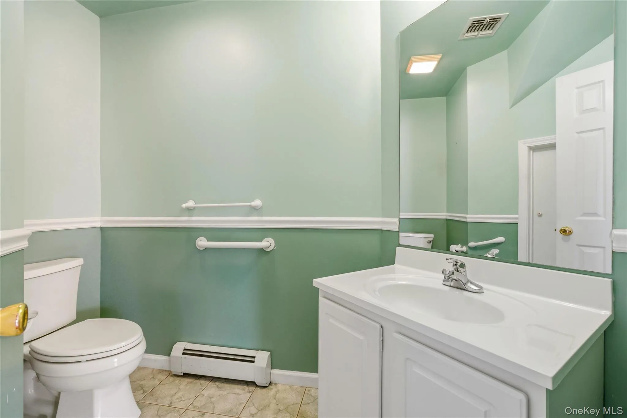 Bathroom featuring a white vanity with integrated sink, chrome faucet, wall-mounted mirror, and tiled flooring Bathroom featuring a white vanity with integrated sink, chrome faucet, wall-mounted mirror, and tiled flooring