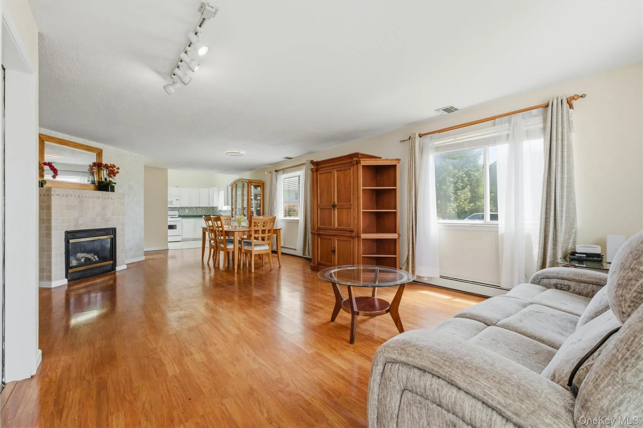 Hardwood-finish flooring throughout, featuring a tiled fireplace with mantel, track lighting, and abundant natural light from multiple windows Hardwood-finish flooring throughout, featuring a tiled fireplace with mantel, track lighting, and abundant natural light from multiple windows