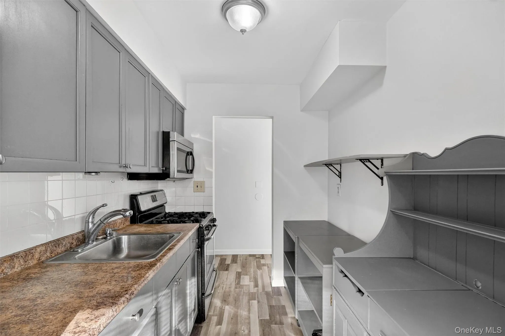 Kitchen featuring appliances with stainless steel finishes, decorative backsplash, light wood-style floors, gray cabinetry, and dark countertops Kitchen featuring appliances with stainless steel finishes, decorative backsplash, light wood-style floors, gray cabinetry, and dark countertops