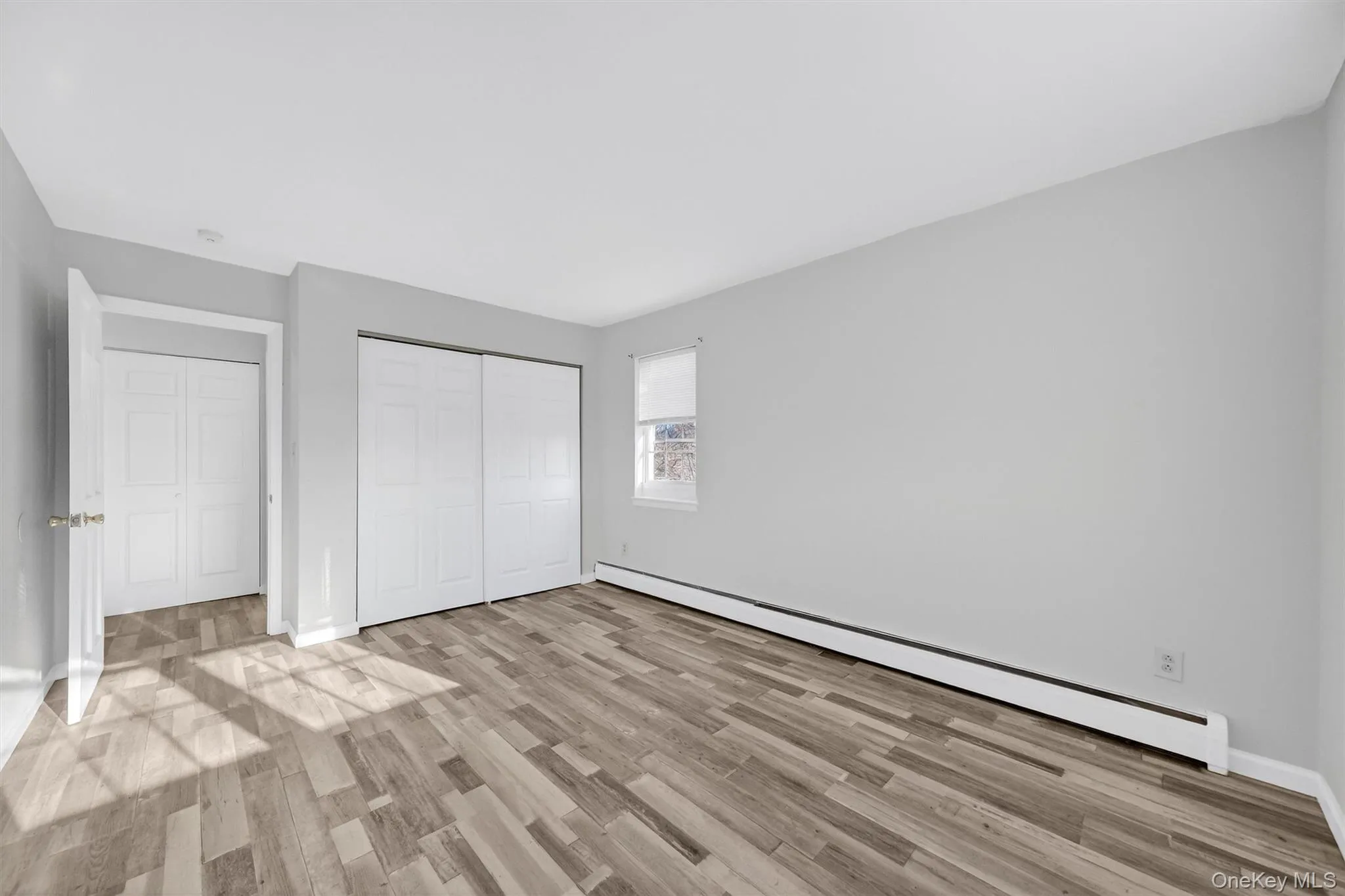 Unfurnished bedroom with a baseboard heating unit, light wood-type flooring, and a closet Unfurnished bedroom with a baseboard heating unit, light wood-type flooring, and a closet
