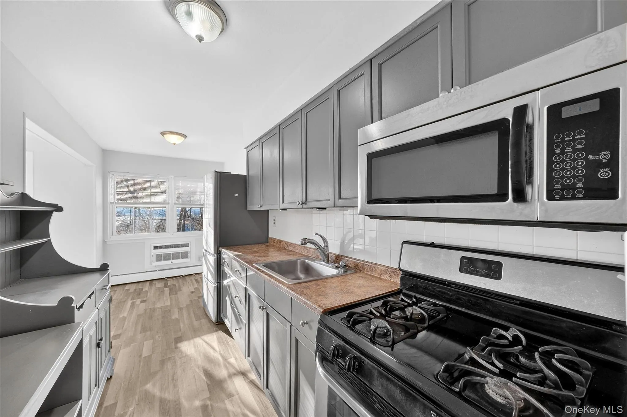 Kitchen with stainless steel appliances, gray cabinetry, light wood-style flooring, decorative backsplash, and baseboard heating Kitchen with stainless steel appliances, gray cabinetry, light wood-style flooring, decorative backsplash, and baseboard heating