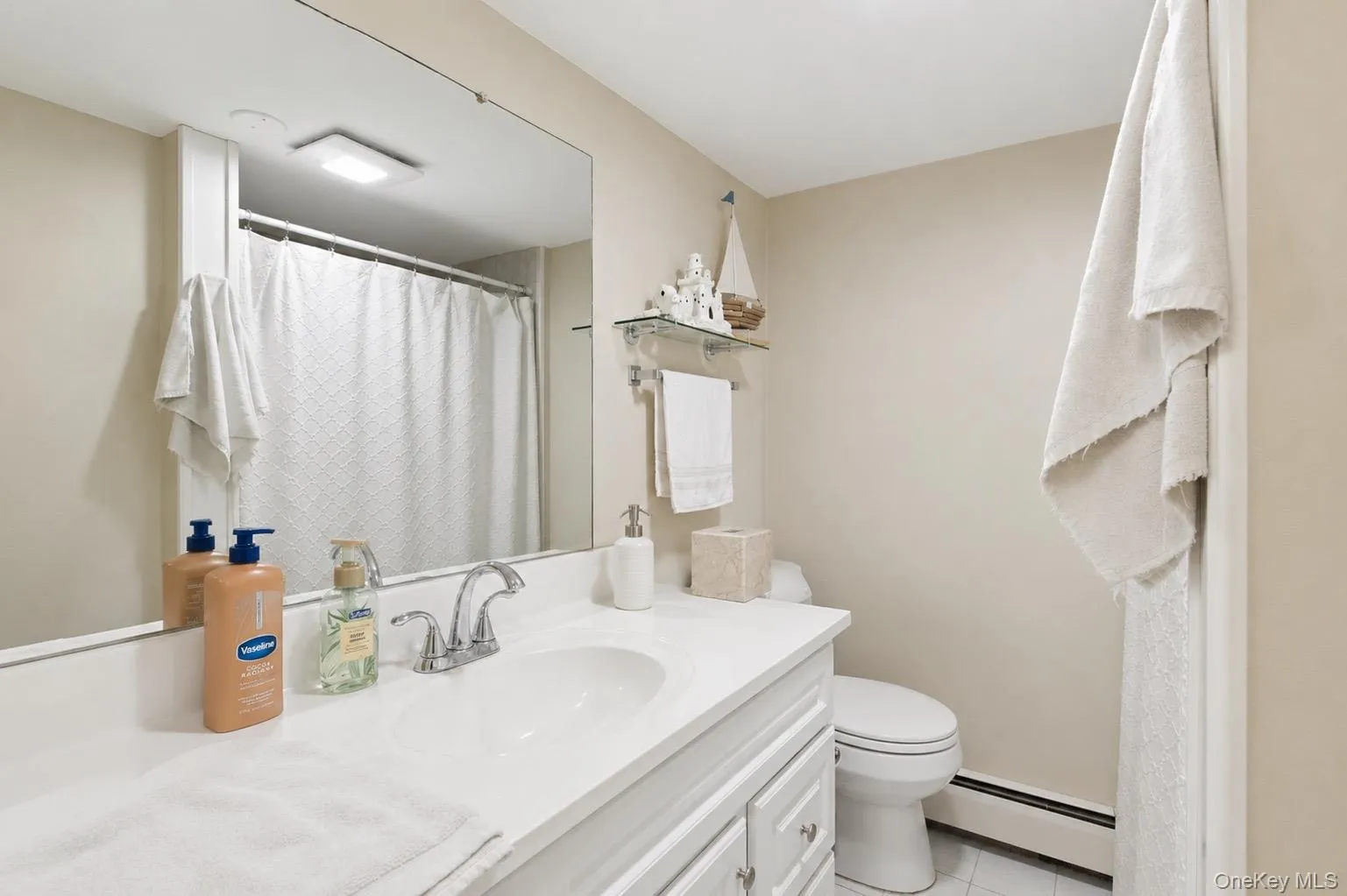 Bathroom featuring a white vanity with an integrated sink, polished chrome faucet, and a large wall-mounted mirror Bathroom featuring a white vanity with an integrated sink, polished chrome faucet, and a large wall-mounted mirror