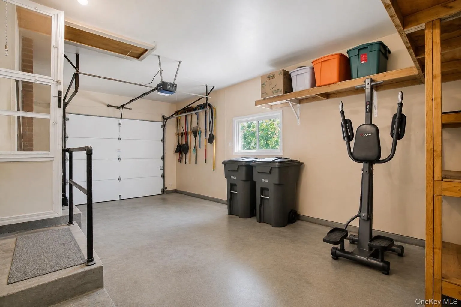 Spacious garage featuring a concrete floor, built-in shelving, a single garage door, and an overhead lighting fixture Spacious garage featuring a concrete floor, built-in shelving, a single garage door, and an overhead lighting fixture