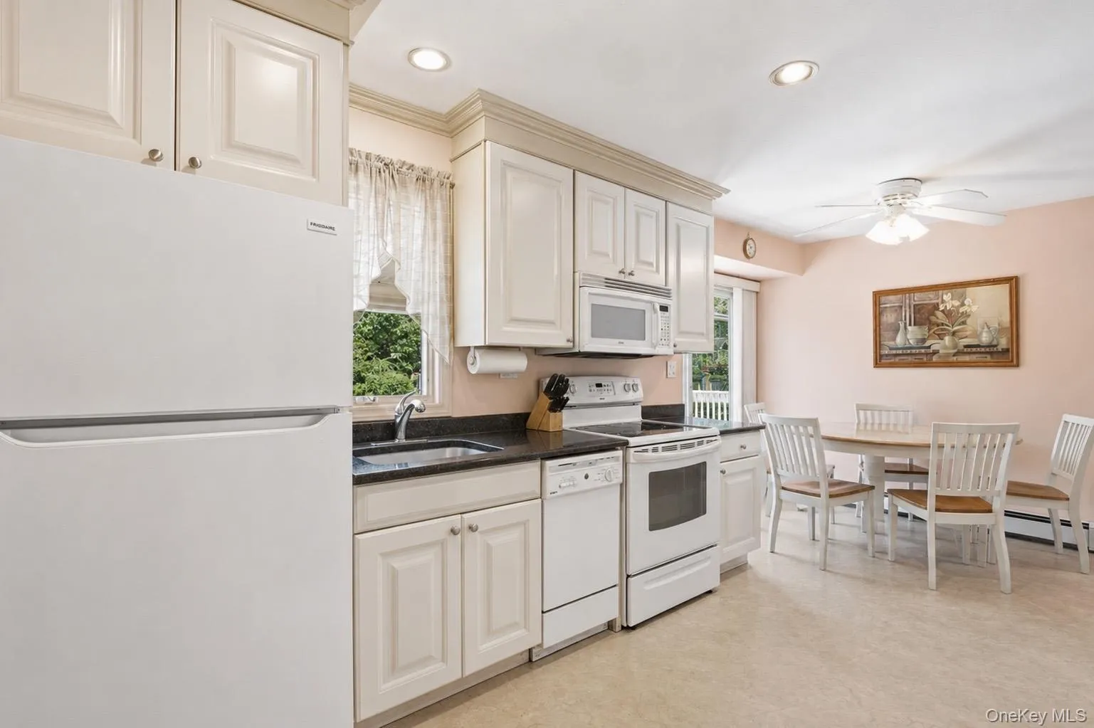 Kitchen featuring white cabinetry, dark countertops, and white appliances Kitchen featuring white cabinetry, dark countertops, and white appliances