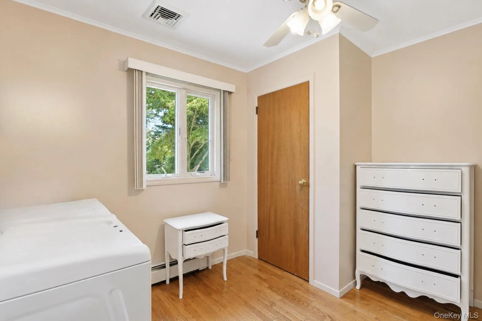 Room featuring wood-finish flooring, a double-hung window, crown molding, a ceiling fan with integrated lighting, and a solid wood door Room featuring wood-finish flooring, a double-hung window, crown molding, a ceiling fan with integrated lighting, and a solid wood door