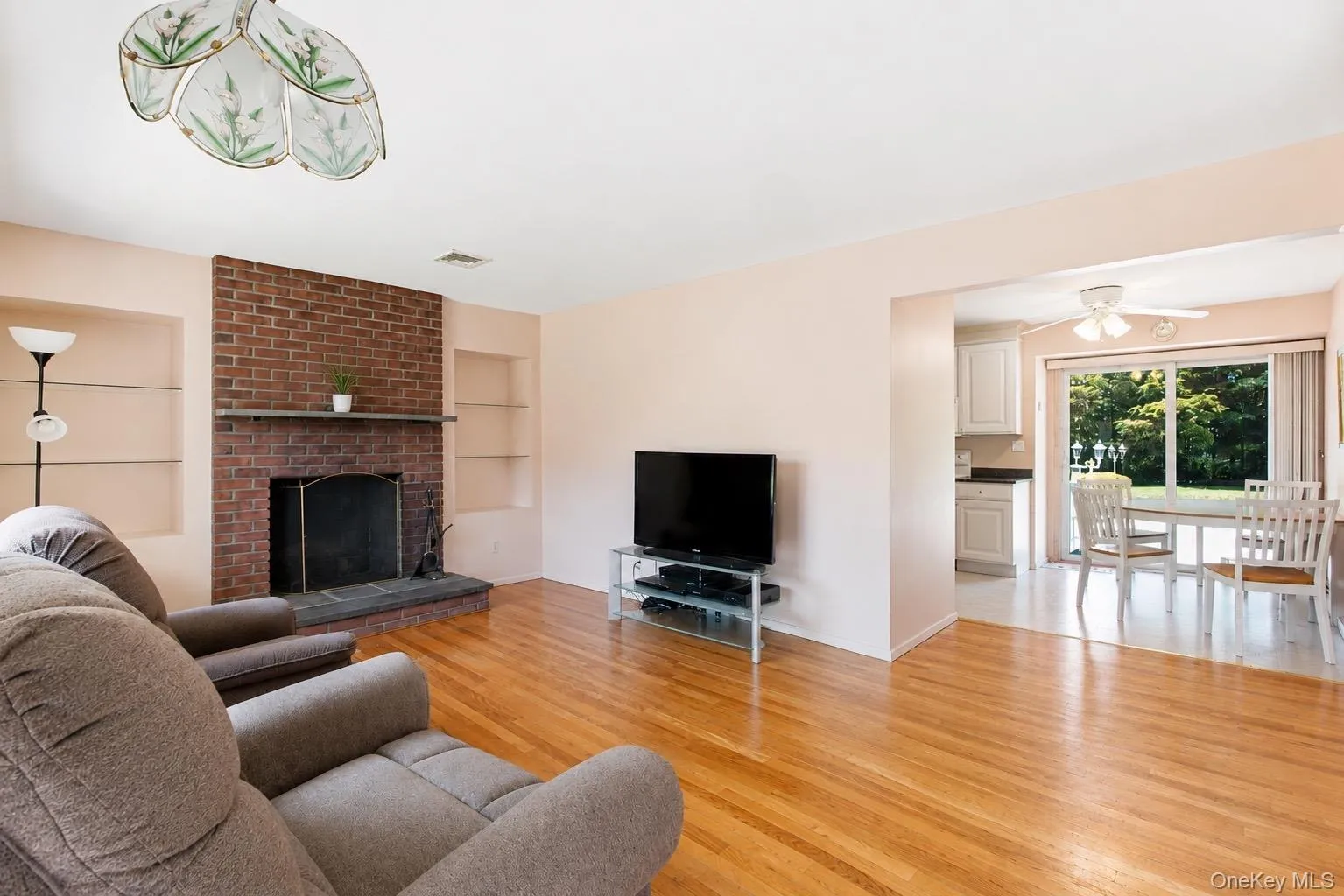 Hardwood flooring throughout featuring a brick fireplace with a stone hearth and mantel Hardwood flooring throughout featuring a brick fireplace with a stone hearth and mantel