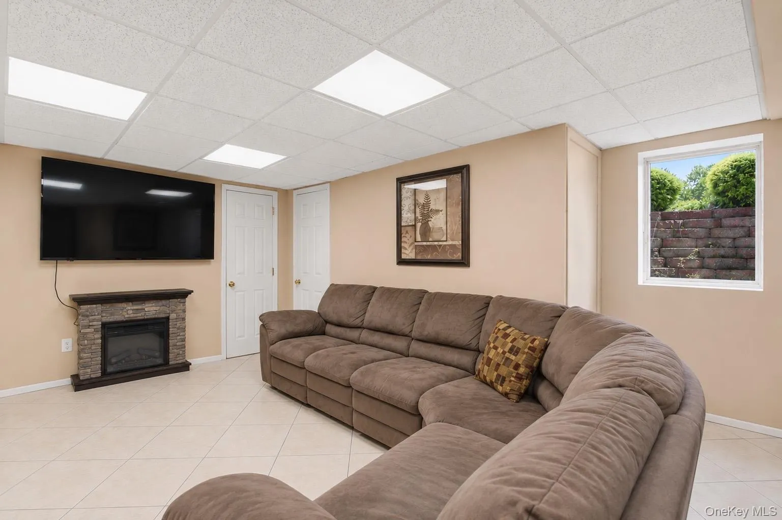 Entertainment space featuring a stone-faced electric fireplace, drop ceiling with recessed lighting, and tile flooring egress windows Entertainment space featuring a stone-faced electric fireplace, drop ceiling with recessed lighting, and tile flooring egress windows