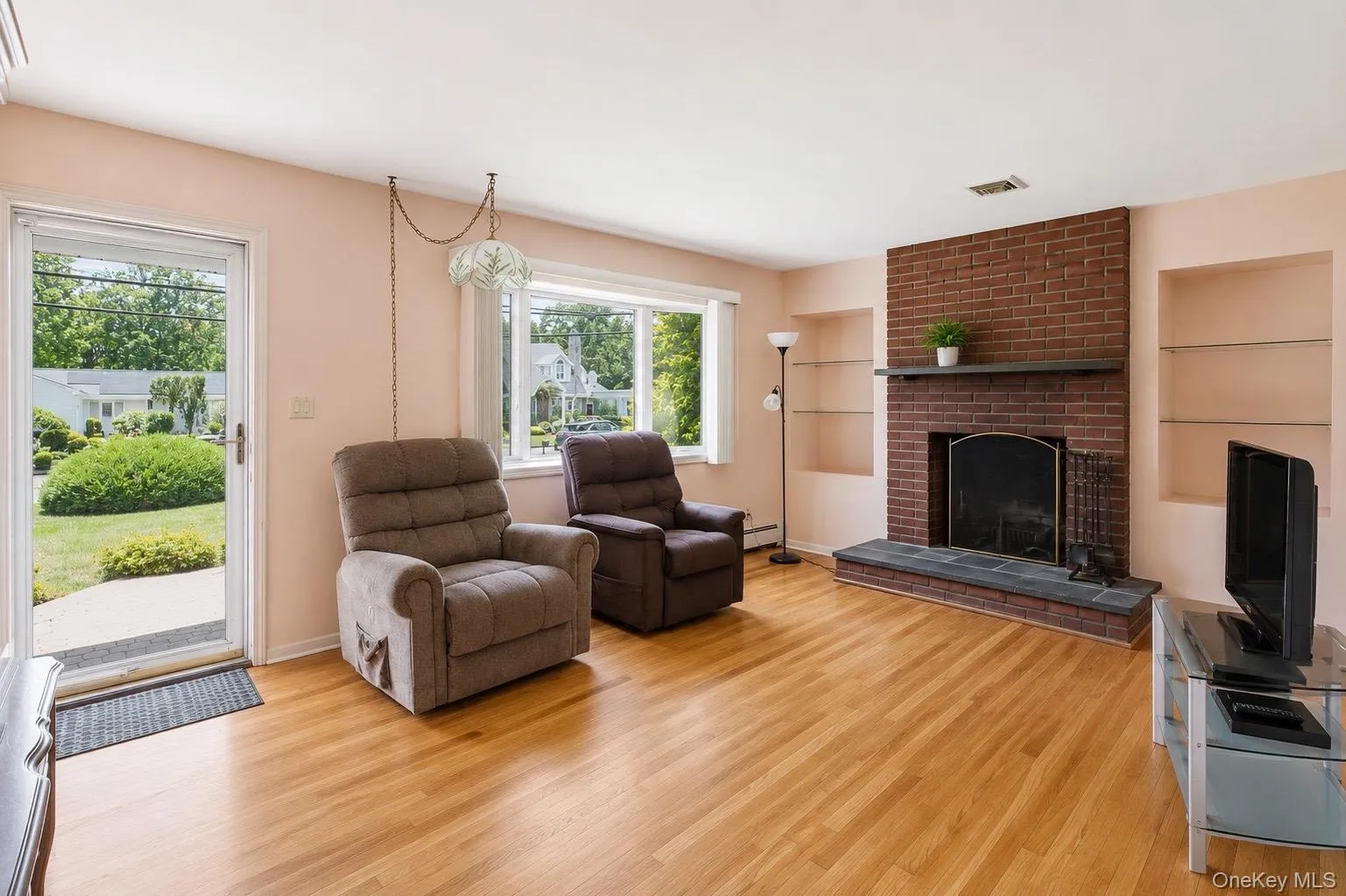 Living area featuring wood-finish flooring, a brick fireplace with a stone hearth, built-in shelving, and large windows Living area featuring wood-finish flooring, a brick fireplace with a stone hearth, built-in shelving, and large windows