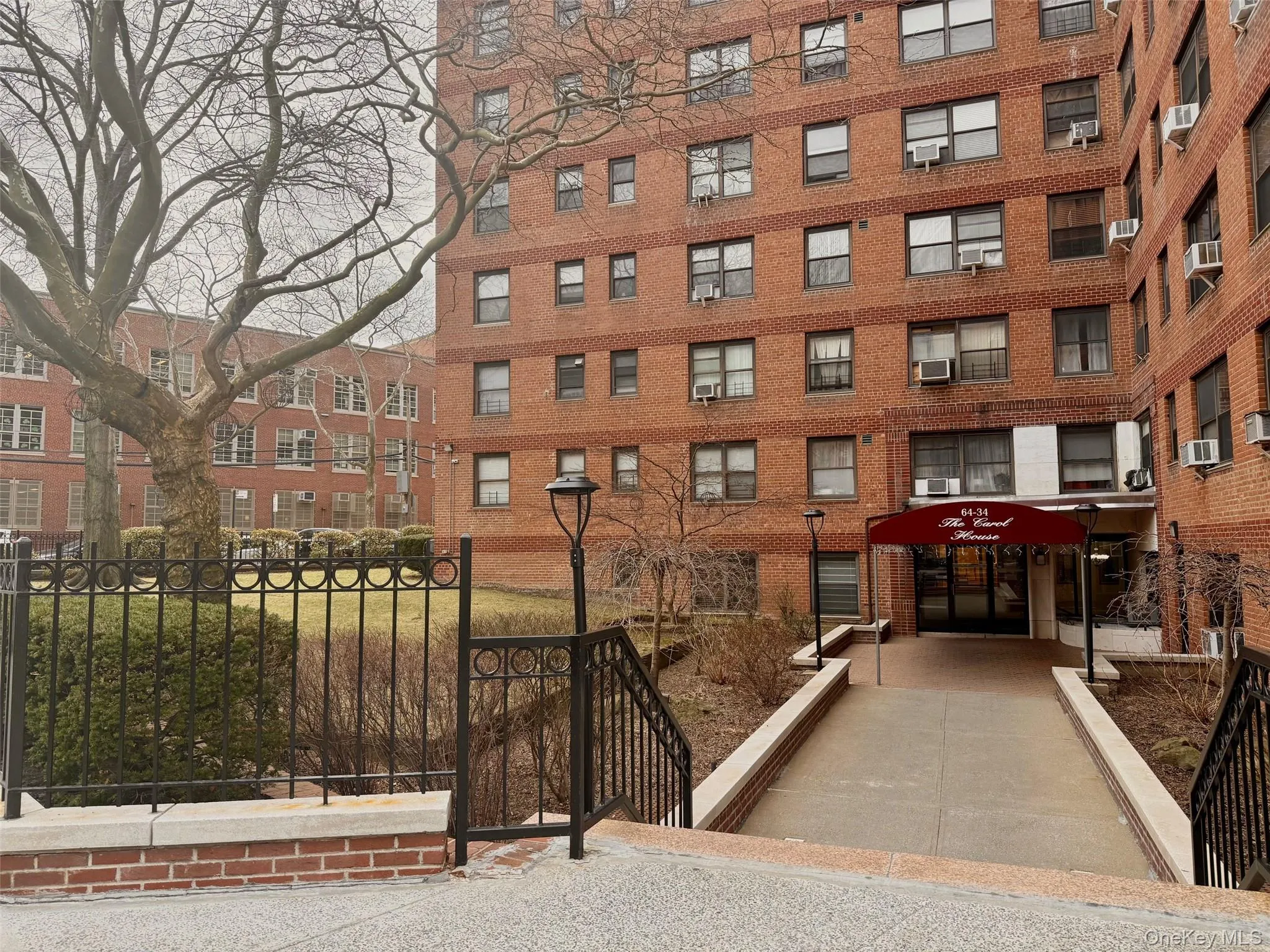 Brick facade building featuring multiple window styles, a covered main entrance, and decorative wrought iron fencing Brick facade building featuring multiple window styles, a covered main entrance, and decorative wrought iron fencing