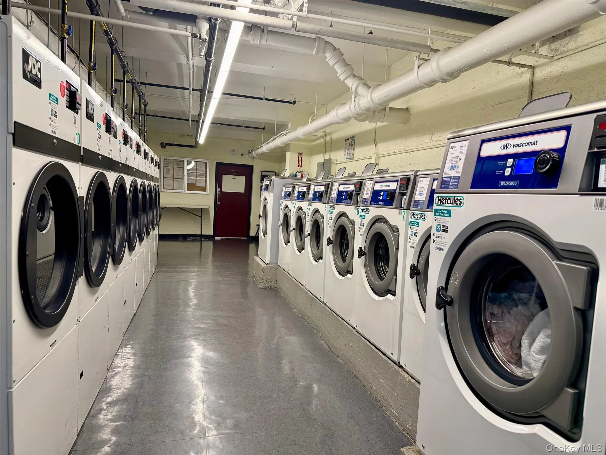 Community laundry room featuring multiple front-loading washing machines, durable flooring, and overhead fluorescent lighting Community laundry room featuring multiple front-loading washing machines, durable flooring, and overhead fluorescent lighting