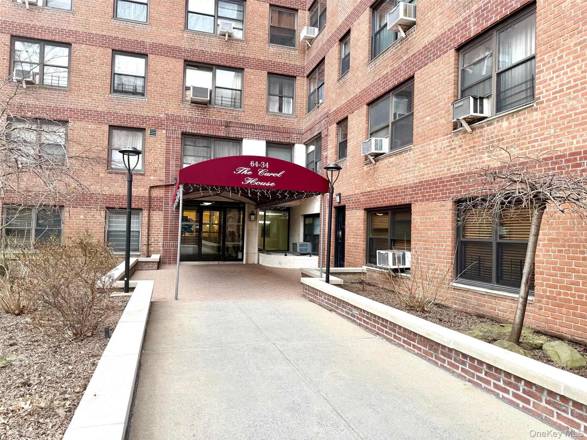 Brick facade building featuring multiple window styles, a covered main entrance, and decorative wrought iron fencing Brick facade building featuring multiple window styles, a covered main entrance, and decorative wrought iron fencing