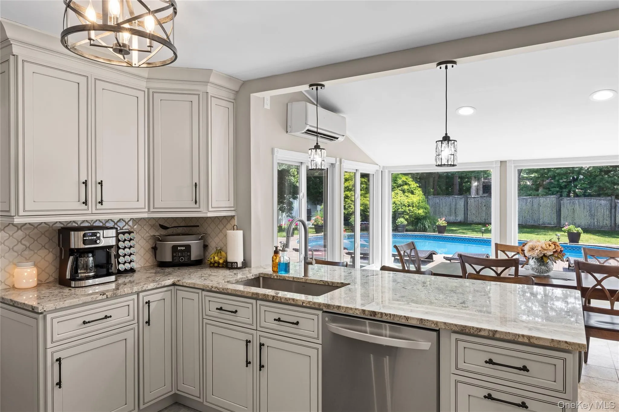 Modern kitchen featuring light cabinetry with dark hardware, a stainless steel dishwasher, and a stone-finish countertop Modern kitchen featuring light cabinetry with dark hardware, a stainless steel dishwasher, and a stone-finish countertop