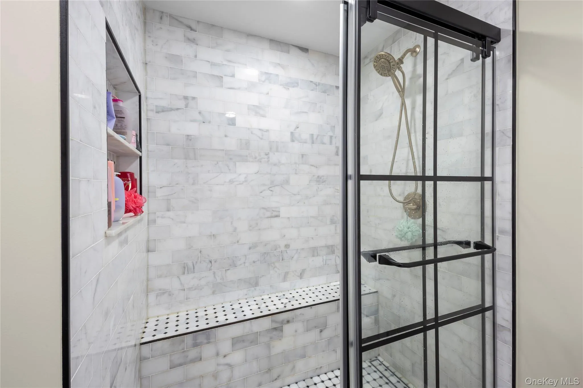 Walk-in shower featuring gray-veined tile walls, a built-in bench with mosaic tile, a recessed niche with shelving, and a glass enclosure with black grid detailing Walk-in shower featuring gray-veined tile walls, a built-in bench with mosaic tile, a recessed niche with shelving, and a glass enclosure with black grid detailing