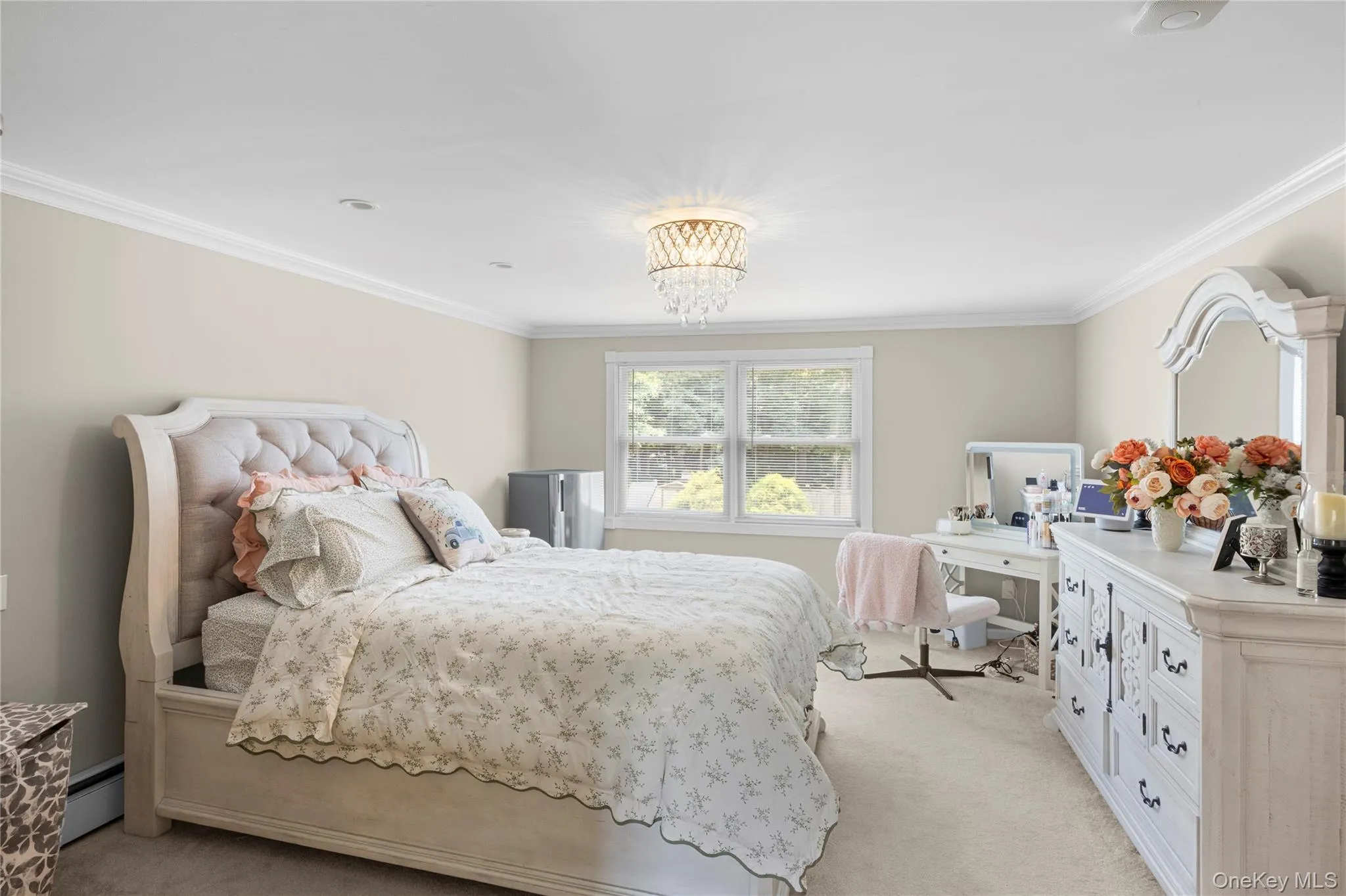 Bedroom featuring a tufted upholstered headboard, crown molding, double windows, a decorative chandelier, and light-colored carpeting Bedroom featuring a tufted upholstered headboard, crown molding, double windows, a decorative chandelier, and light-colored carpeting