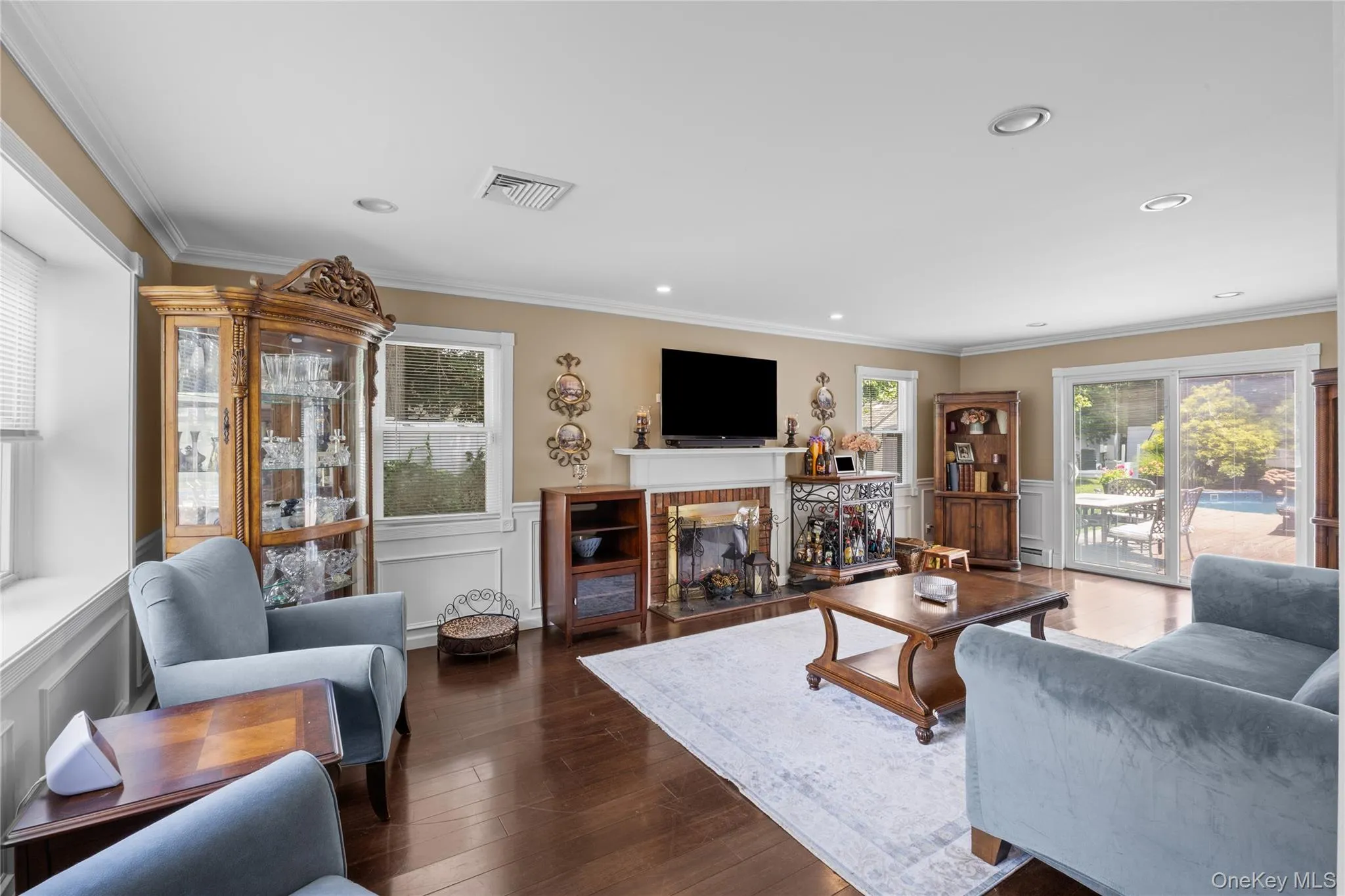 Spacious living area featuring rich wood-finish flooring, a white mantel fireplace with a black stone hearth, crown molding, and recessed lighting Spacious living area featuring rich wood-finish flooring, a white mantel fireplace with a black stone hearth, crown molding, and recessed lighting