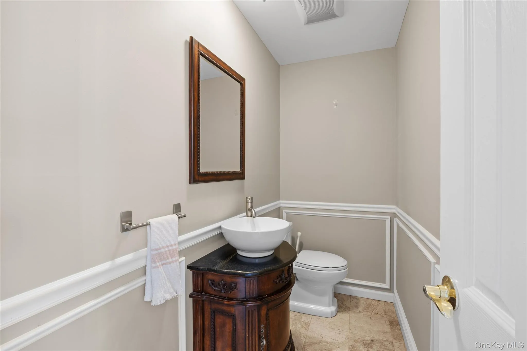 Powder room featuring a dark wood vanity with a vessel sink, a coordinating framed mirror, wainscoting, and tile flooring Powder room featuring a dark wood vanity with a vessel sink, a coordinating framed mirror, wainscoting, and tile flooring