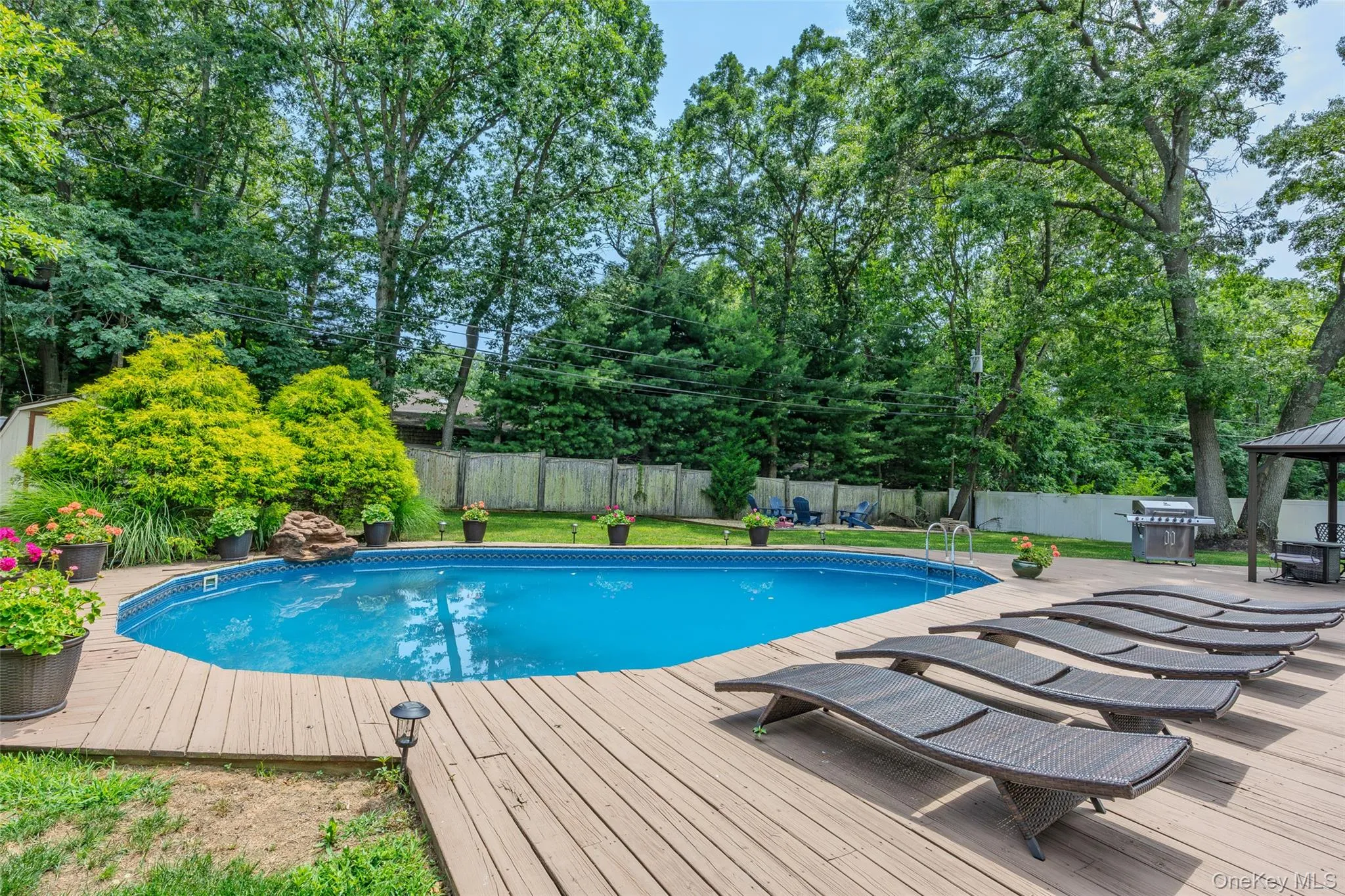 In-ground swimming pool with a surrounding wood deck, bordered by established landscaping and mature trees In-ground swimming pool with a surrounding wood deck, bordered by established landscaping and mature trees