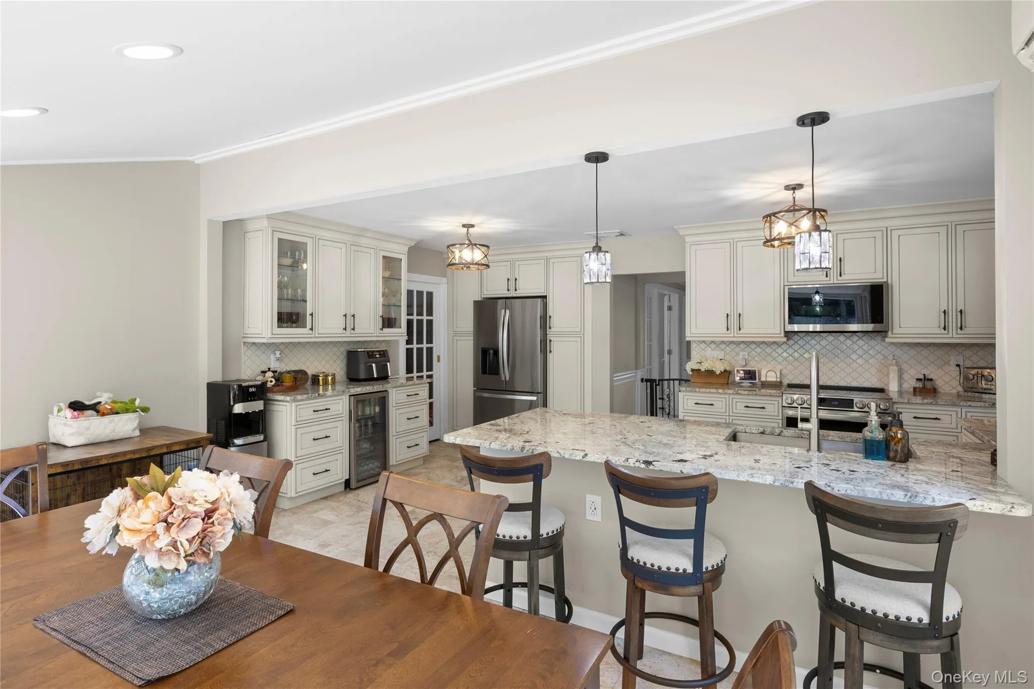 Open-concept kitchen featuring light cabinetry, stainless steel appliances, a multi-level island with seating, and pendant lighting Open-concept kitchen featuring light cabinetry, stainless steel appliances, a multi-level island with seating, and pendant lighting
