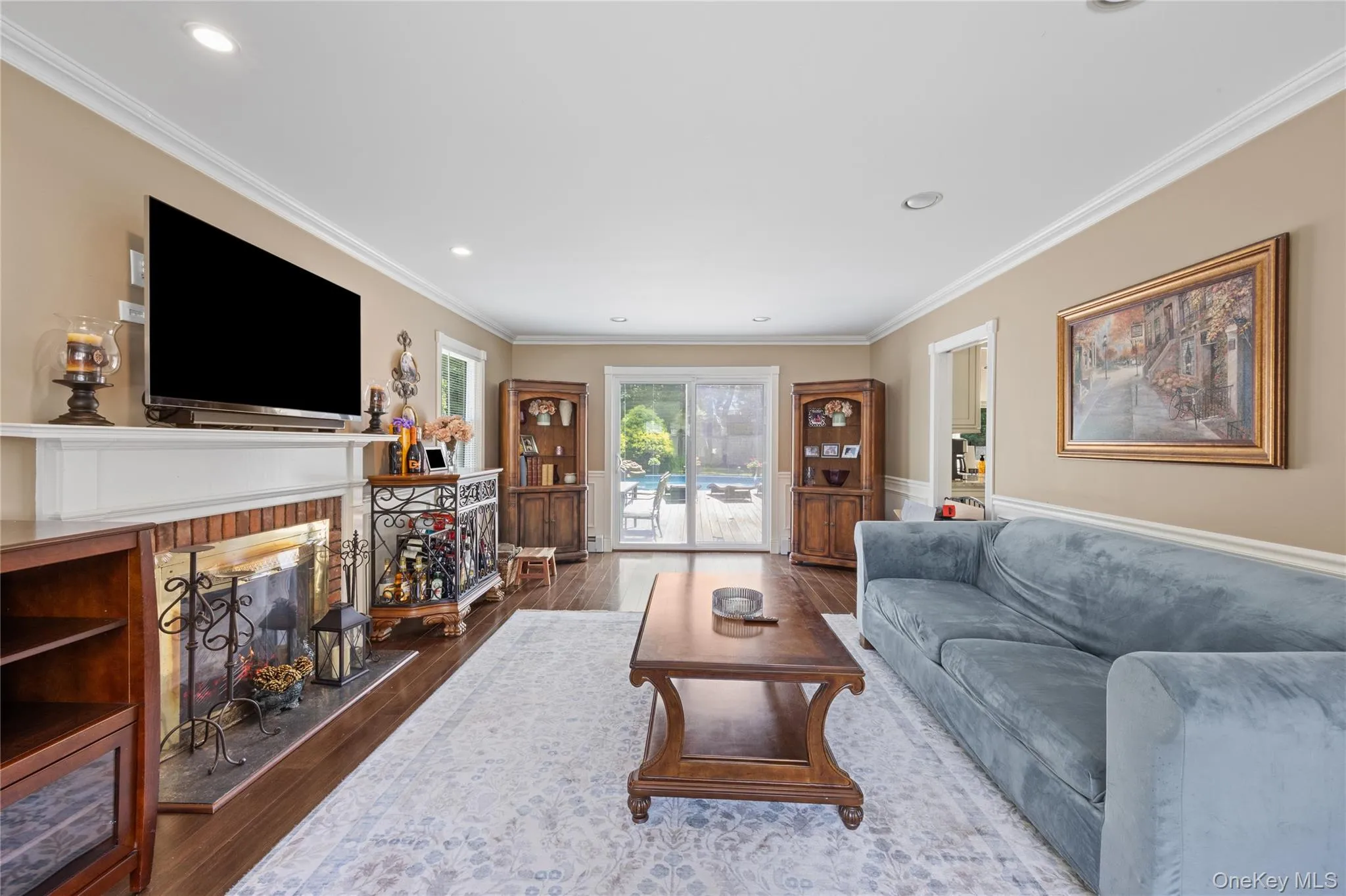 Living area featuring wood-finish flooring, a brick-surround fireplace with a white mantel, and crown molding Living area featuring wood-finish flooring, a brick-surround fireplace with a white mantel, and crown molding