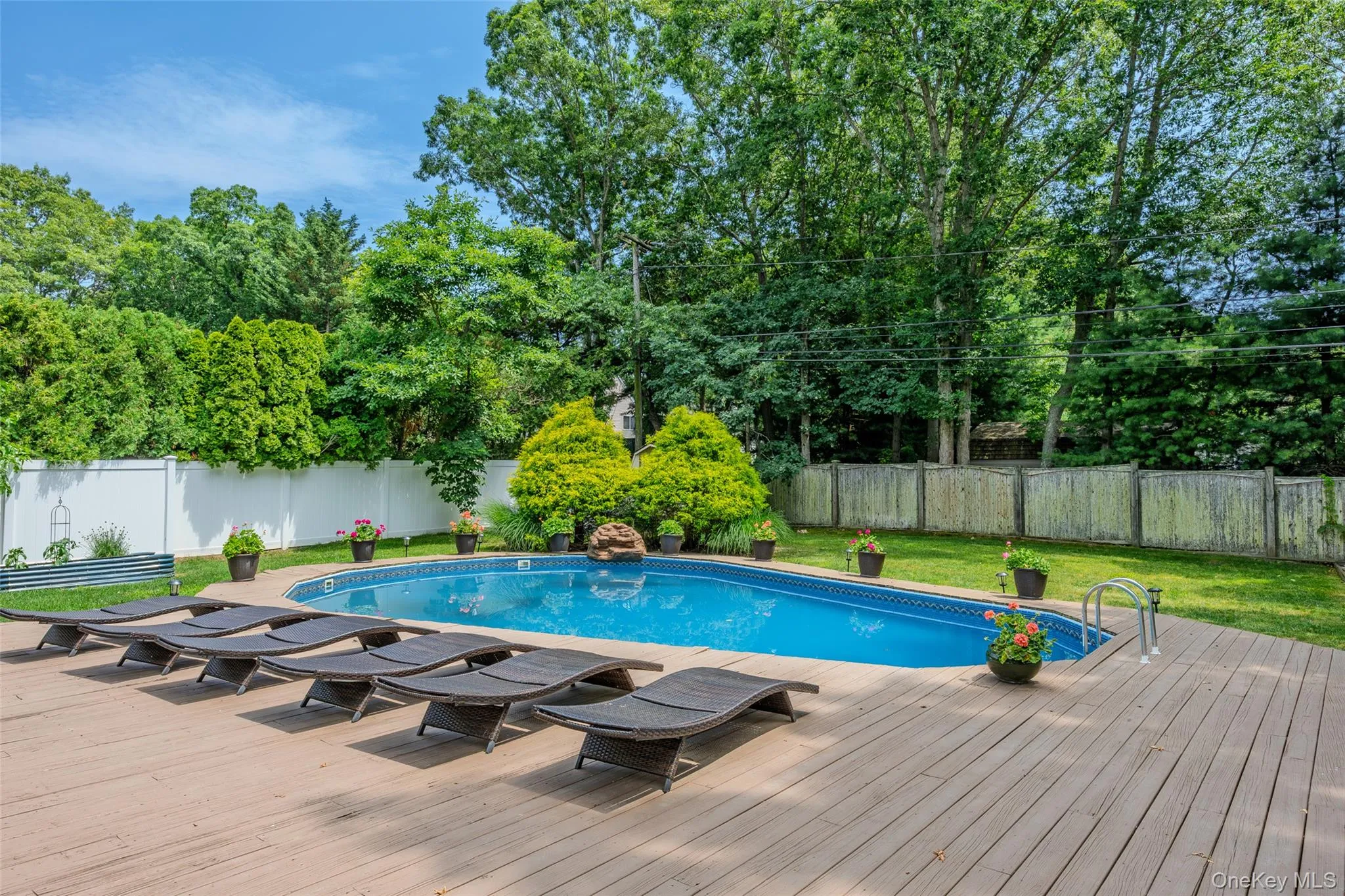 In-ground swimming pool with a surrounding wood-finish deck, bordered by mature trees and privacy fencing In-ground swimming pool with a surrounding wood-finish deck, bordered by mature trees and privacy fencing