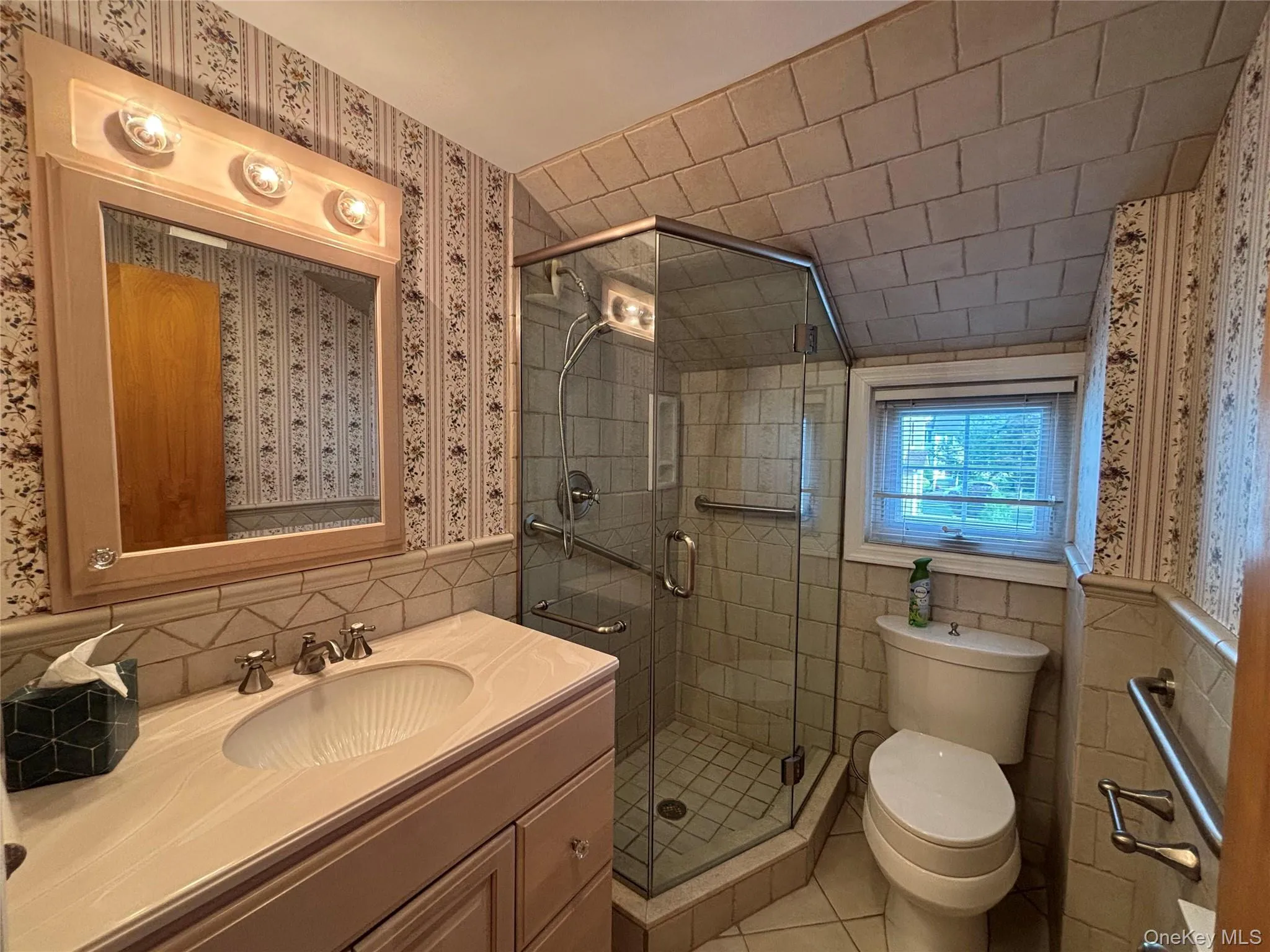 Bathroom featuring a glass-enclosed shower, single vanity with integrated sink, and a framed mirror with overhead lighting Bathroom featuring a glass-enclosed shower, single vanity with integrated sink, and a framed mirror with overhead lighting