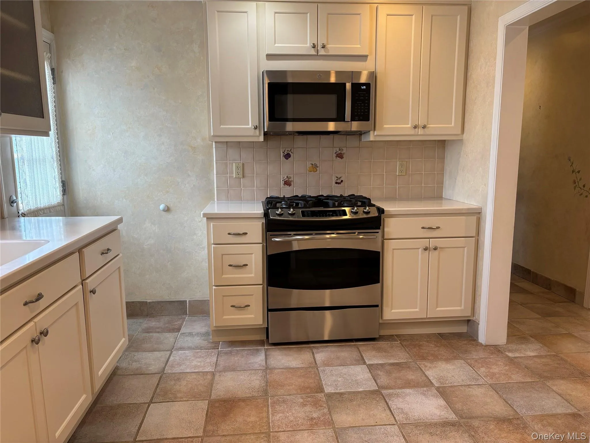 Kitchen featuring white shaker cabinetry, stainless steel range and microwave, light-toned countertops, and a tiled backsplash Kitchen featuring white shaker cabinetry, stainless steel range and microwave, light-toned countertops, and a tiled backsplash