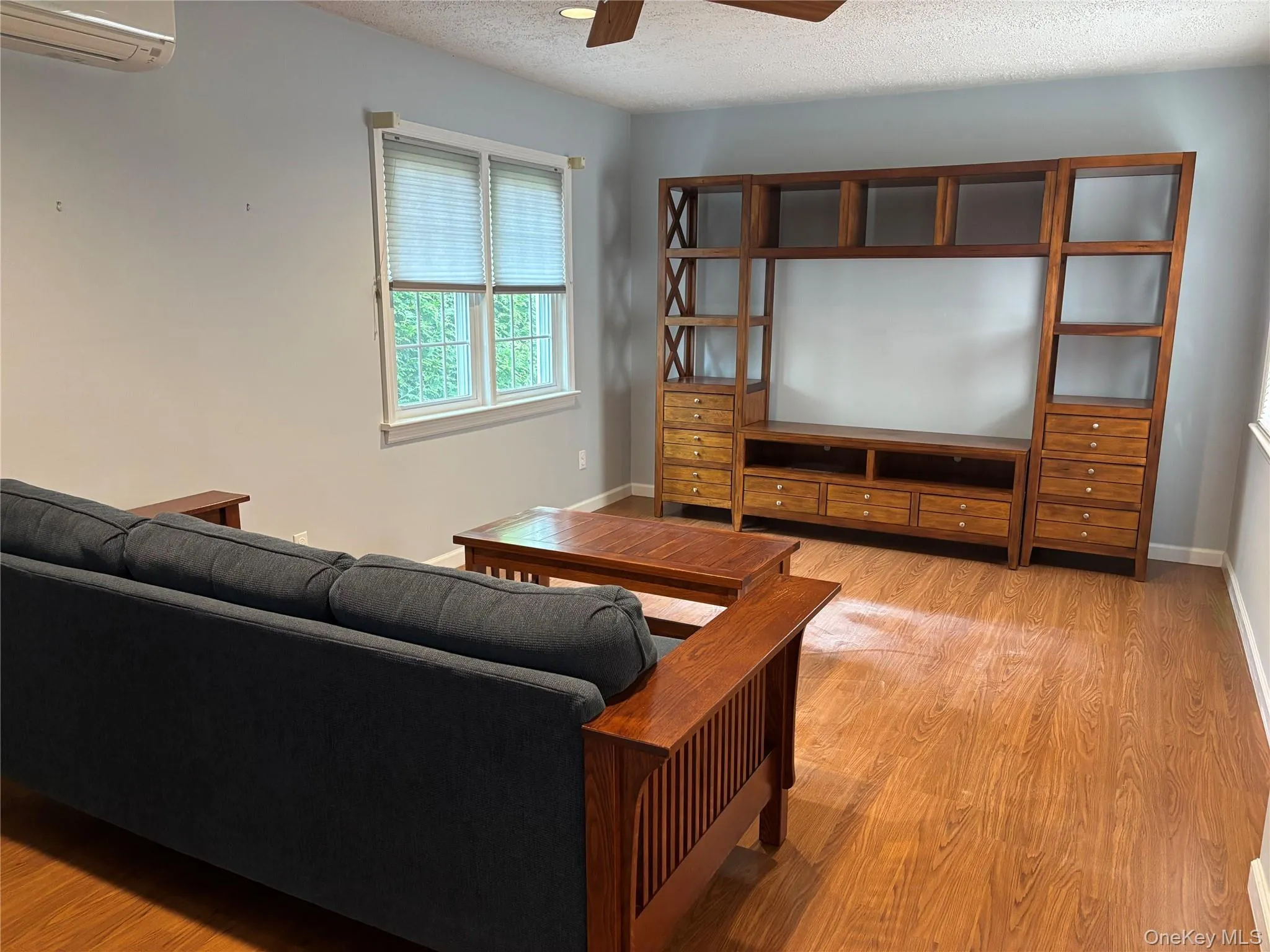 Spacious living area featuring wood-finish flooring, light gray wall paint, and a built-in entertainment center with shelving and drawer storage Spacious living area featuring wood-finish flooring, light gray wall paint, and a built-in entertainment center with shelving and drawer storage