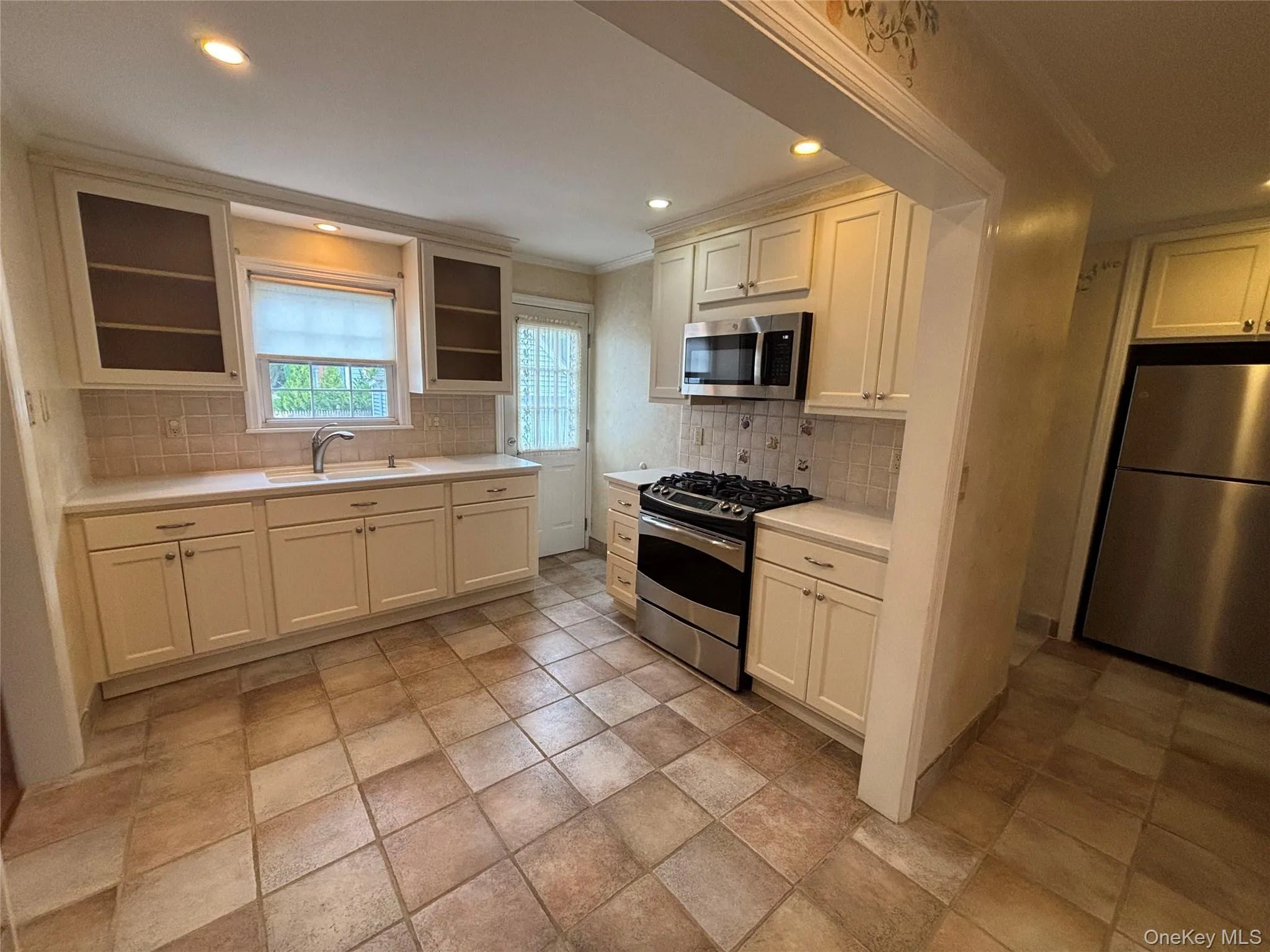 Kitchen featuring cream-colored cabinetry, stainless steel appliances, tiled flooring, light-toned countertops, and a tiled backsplash Kitchen featuring cream-colored cabinetry, stainless steel appliances, tiled flooring, light-toned countertops, and a tiled backsplash