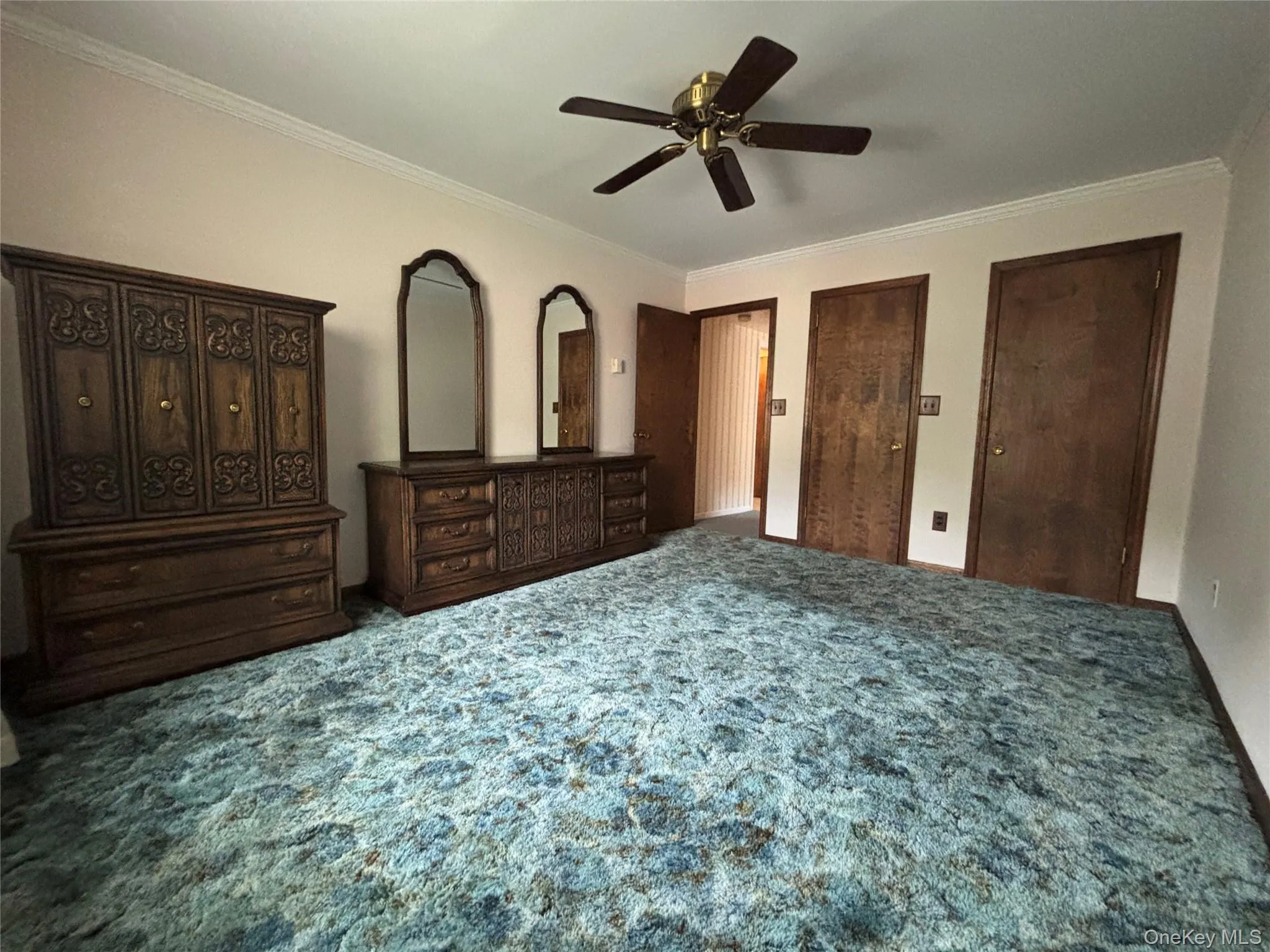 Spacious room featuring broadloom carpeting, a ceiling fan, and multiple wood-paneled doors Spacious room featuring broadloom carpeting, a ceiling fan, and multiple wood-paneled doors