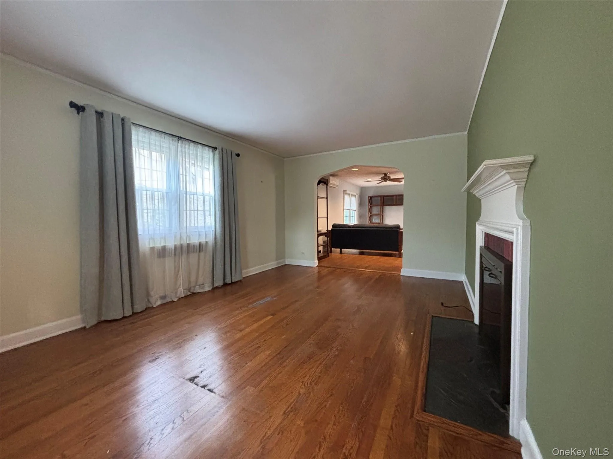 Living area featuring wood-finish flooring, a decorative fireplace with a white mantel, and an arched doorway leading to an additional room Living area featuring wood-finish flooring, a decorative fireplace with a white mantel, and an arched doorway leading to an additional room