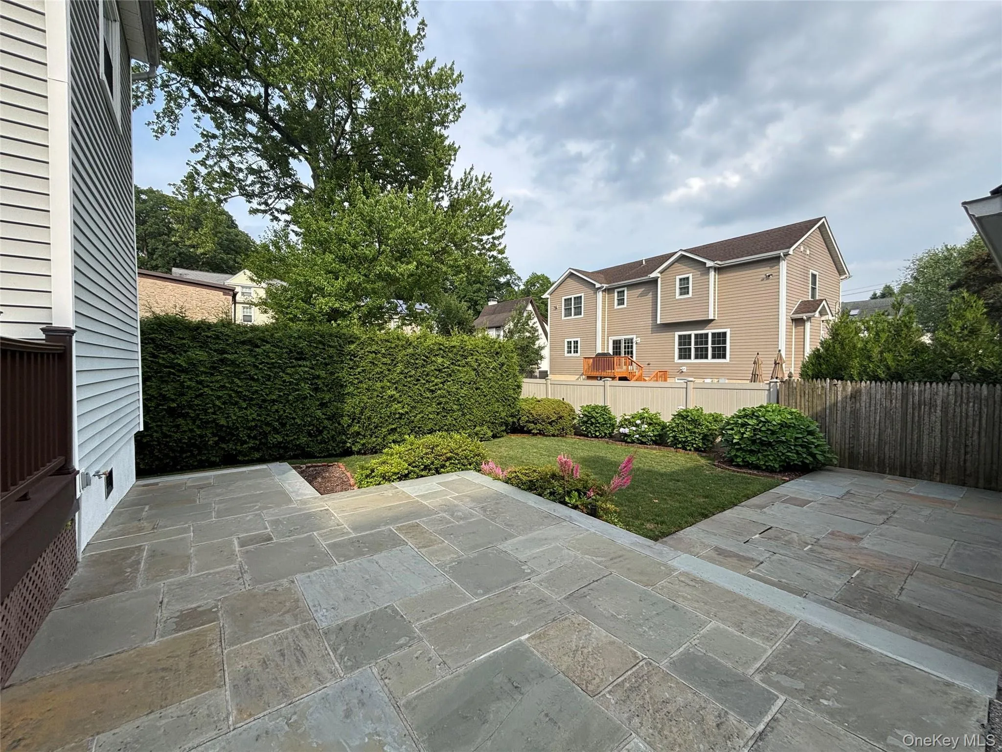 Expansive flagstone patio area featuring a manicured lawn, established perimeter hedging, and mature landscaping Expansive flagstone patio area featuring a manicured lawn, established perimeter hedging, and mature landscaping